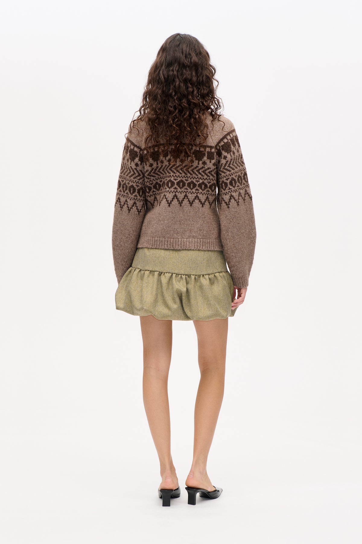 Back view of a model wearing a taupe knit sweater with dark brown geometric bands and a gathered olive mini skirt.
