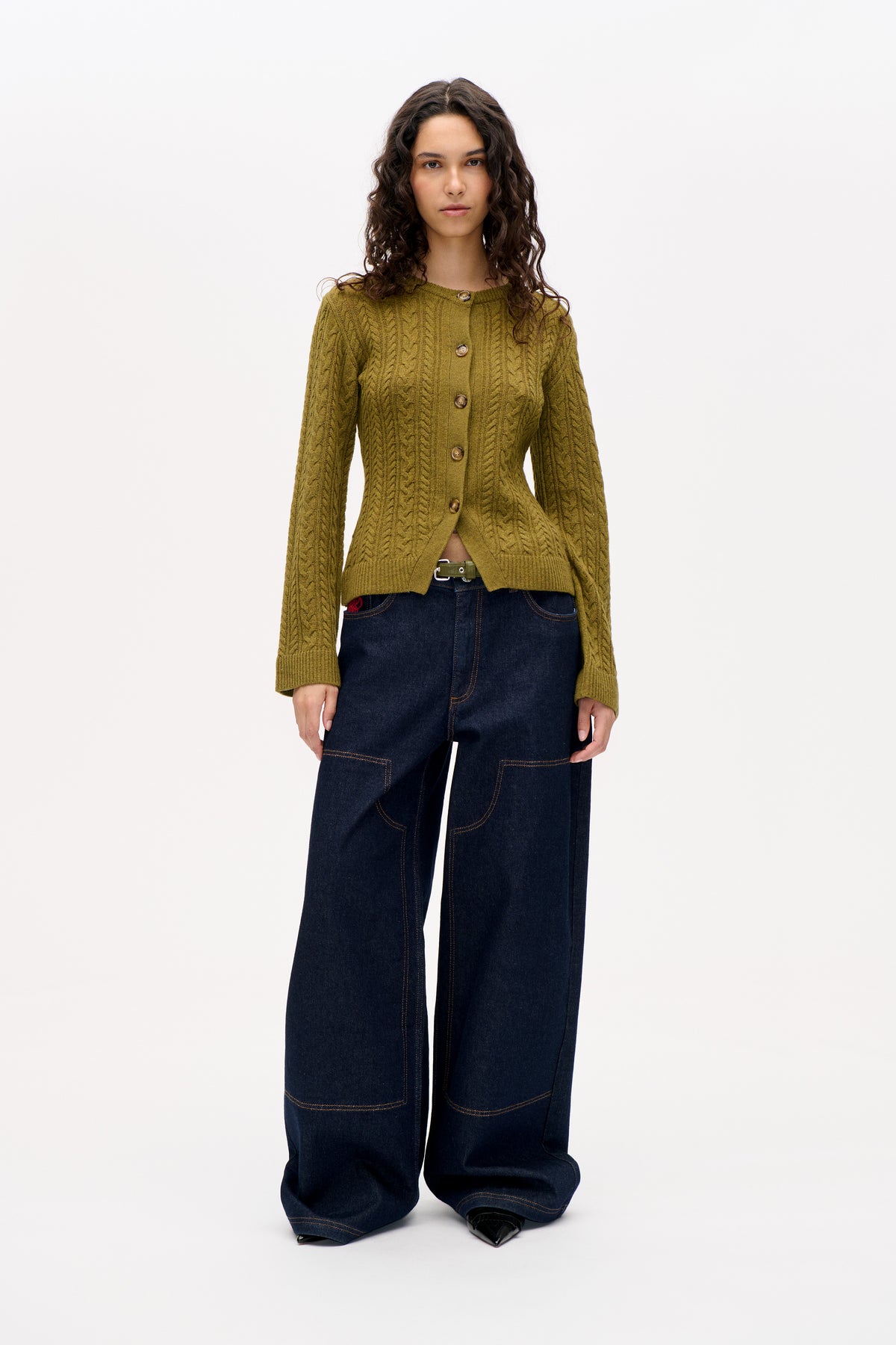 Front view of a model wearing an olive green cable-knit cardigan with buttons and dark wide-leg jeans.
