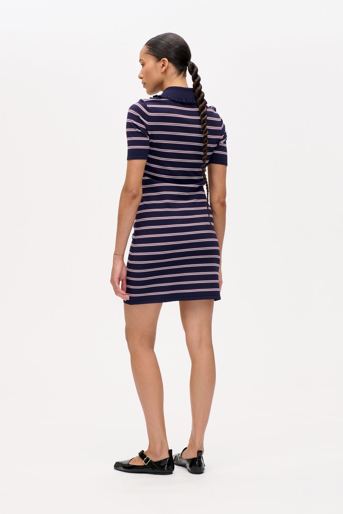 Back view of a model wearing a navy short-sleeved mini dress with thin white and burgundy horizontal stripes and a ruffled collar.