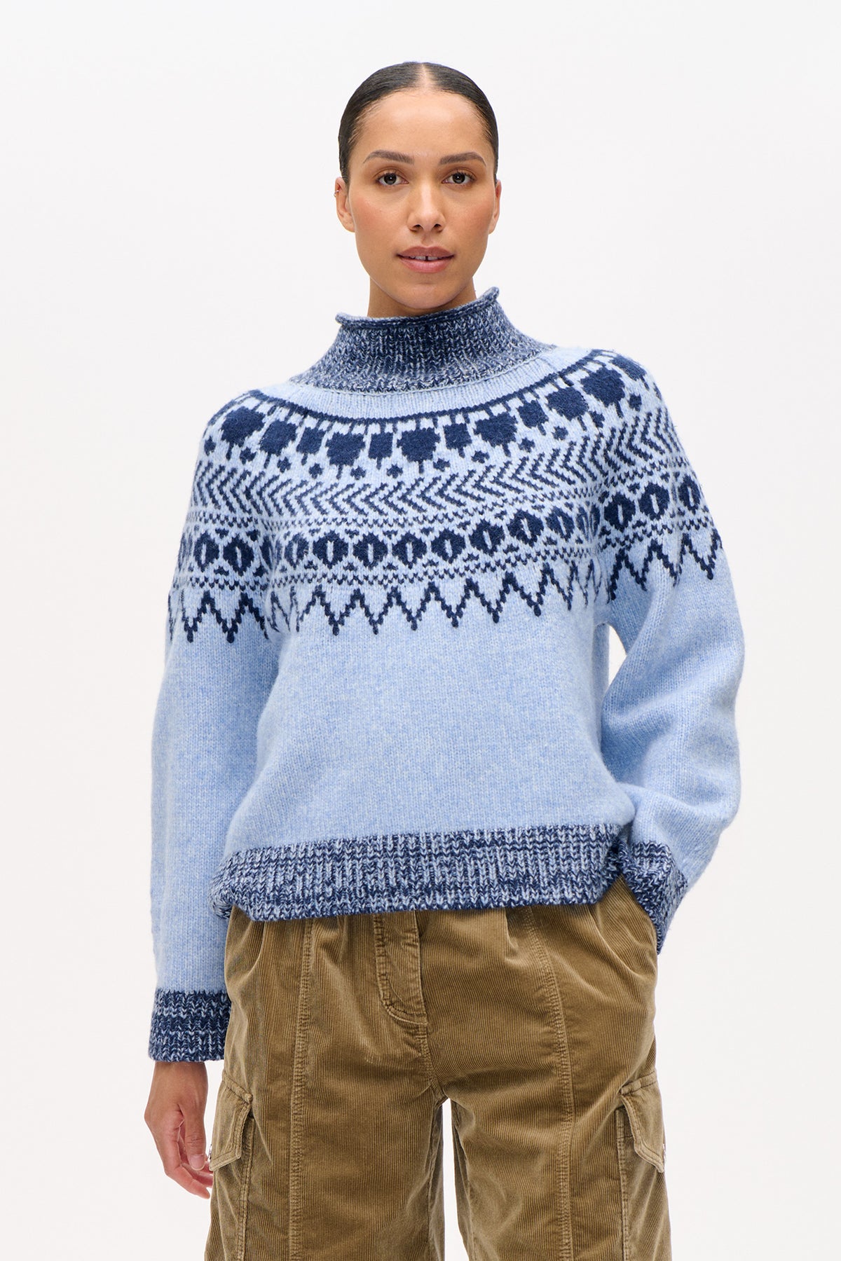 Front view of a model wearing a pale blue knit sweater with a high ribbed neck and navy geometric pattern across the shoulders.