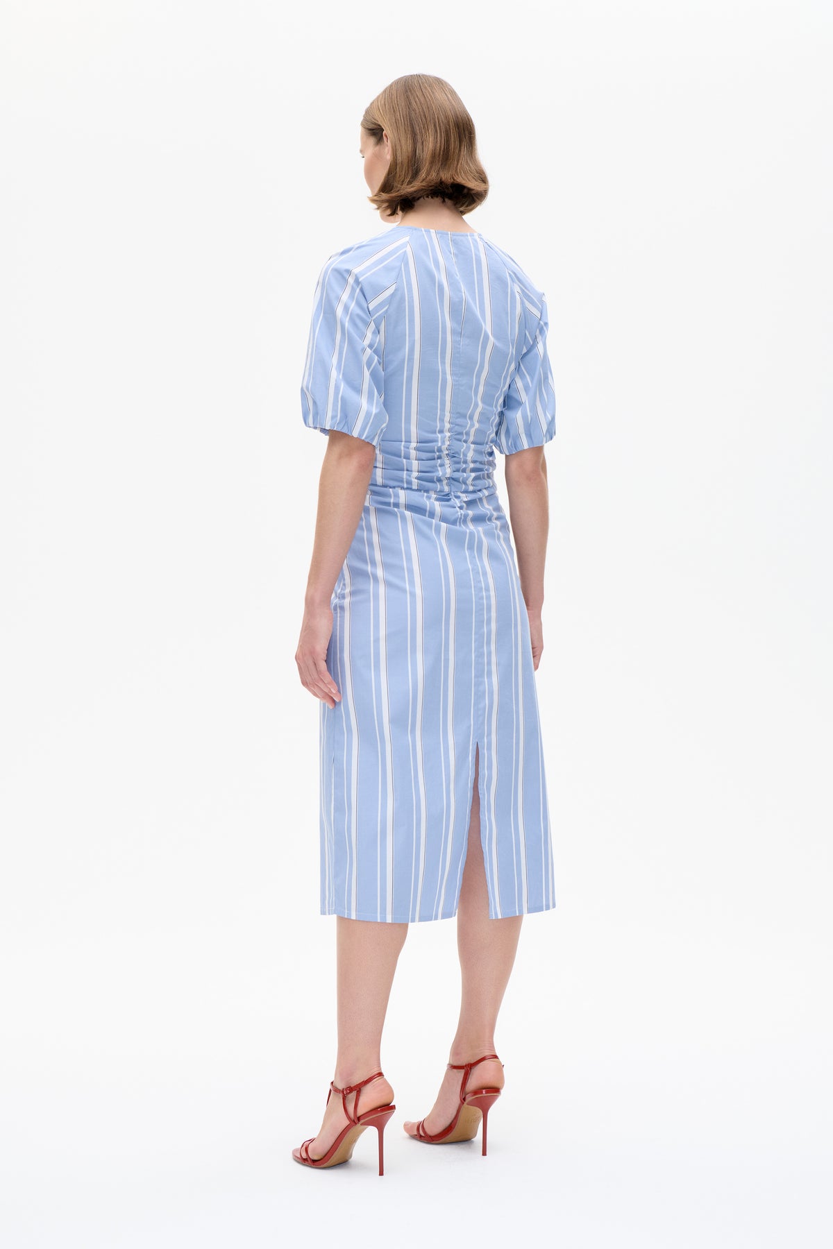 Back view of a light blue dress with white vertical stripes, puff sleeves, a gathered waist and a skirt slit.