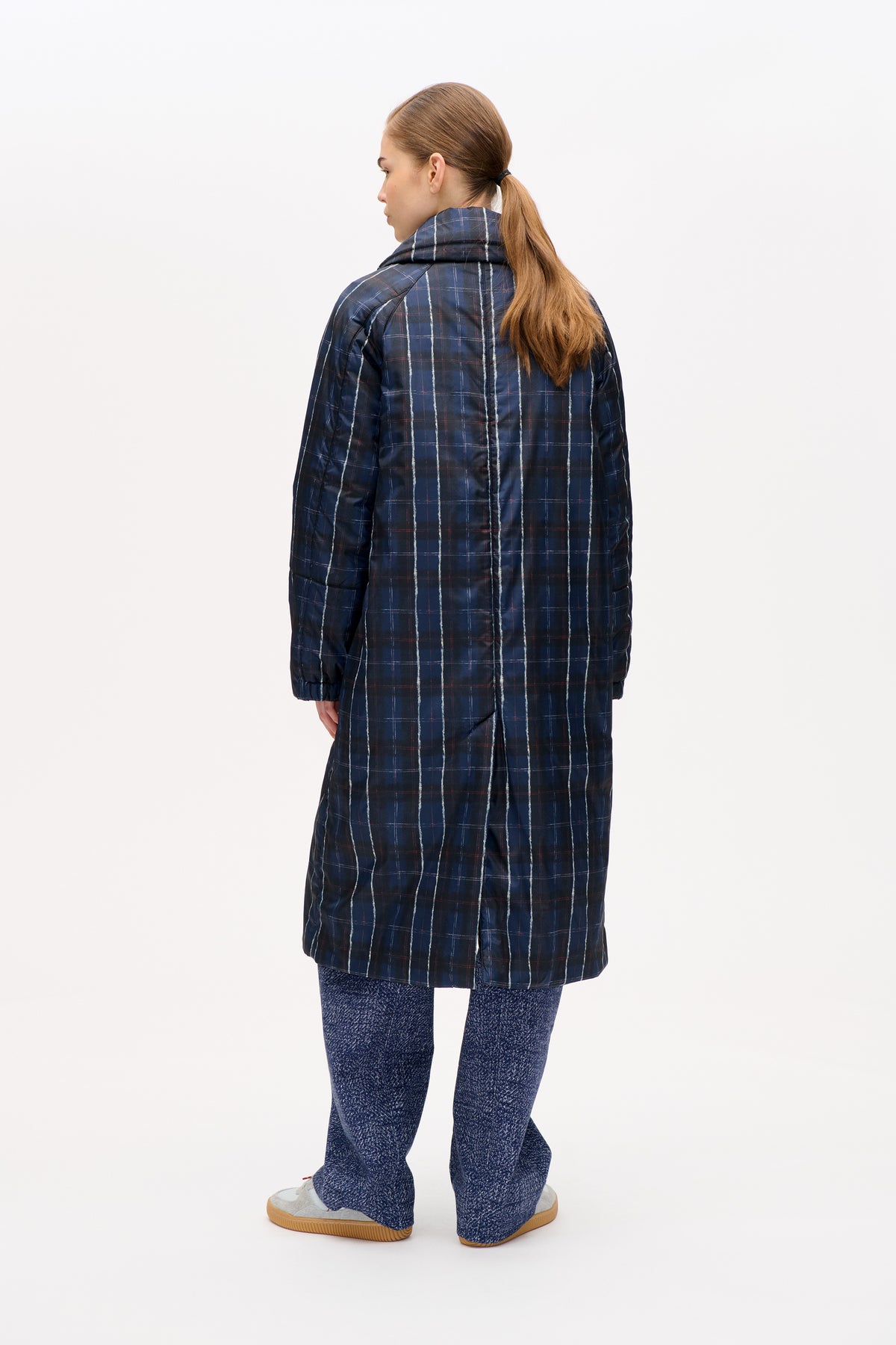 Back view of a long navy padded coat with a high collar and white and red plaid pattern.