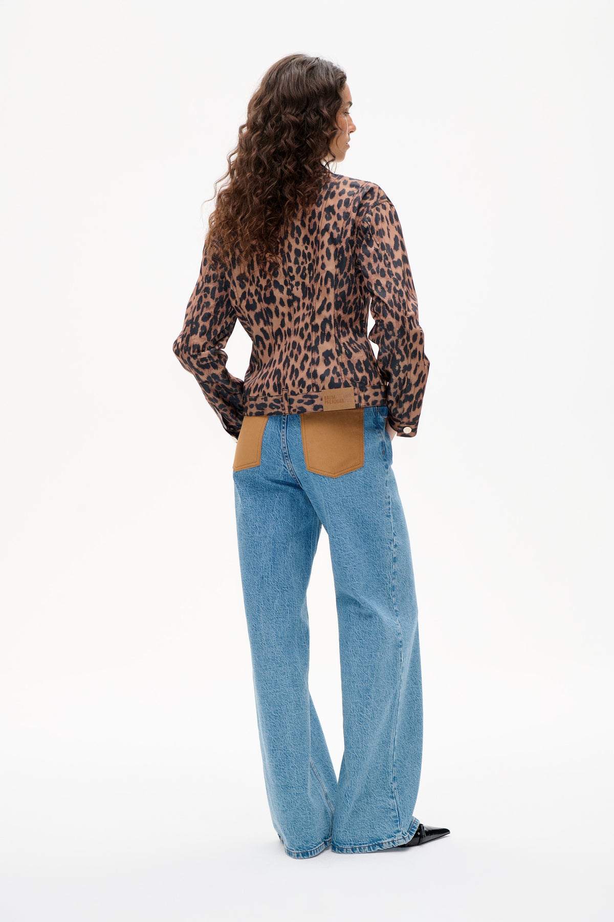Rückenansicht einer braun-schwarzen Jacke mit Leopardenmuster und beigen Aufnähern, kombiniert mit blauen Jeans.
