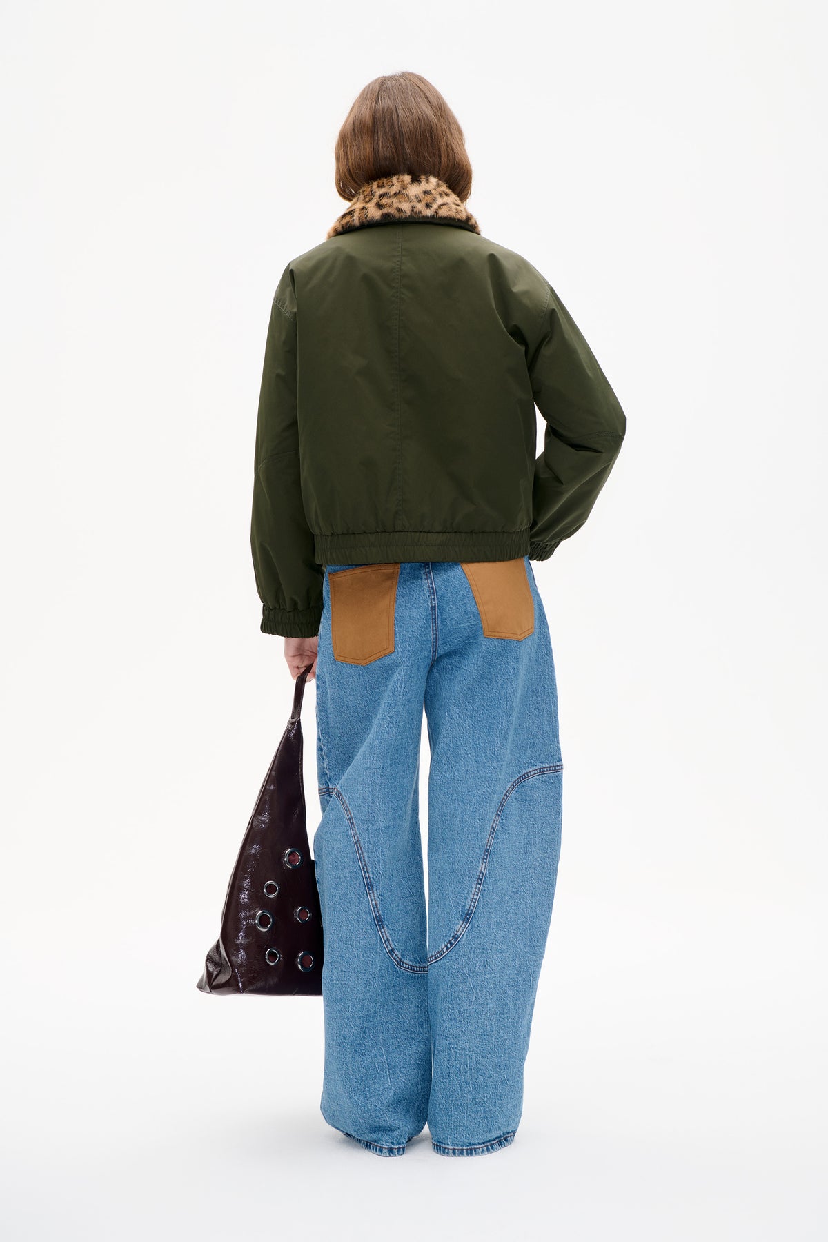 Back view of a dark olive jacket with an elasticated hem and cuffs and a tan-and-black animal-print collar, styled with blue jeans.
