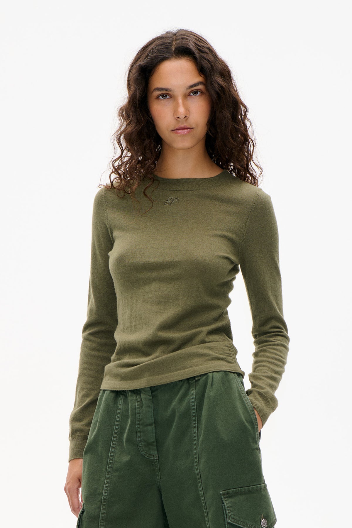 Front view of a model wearing an olive green long-sleeved crew-neck top with a small chest emblem and dark green trousers.