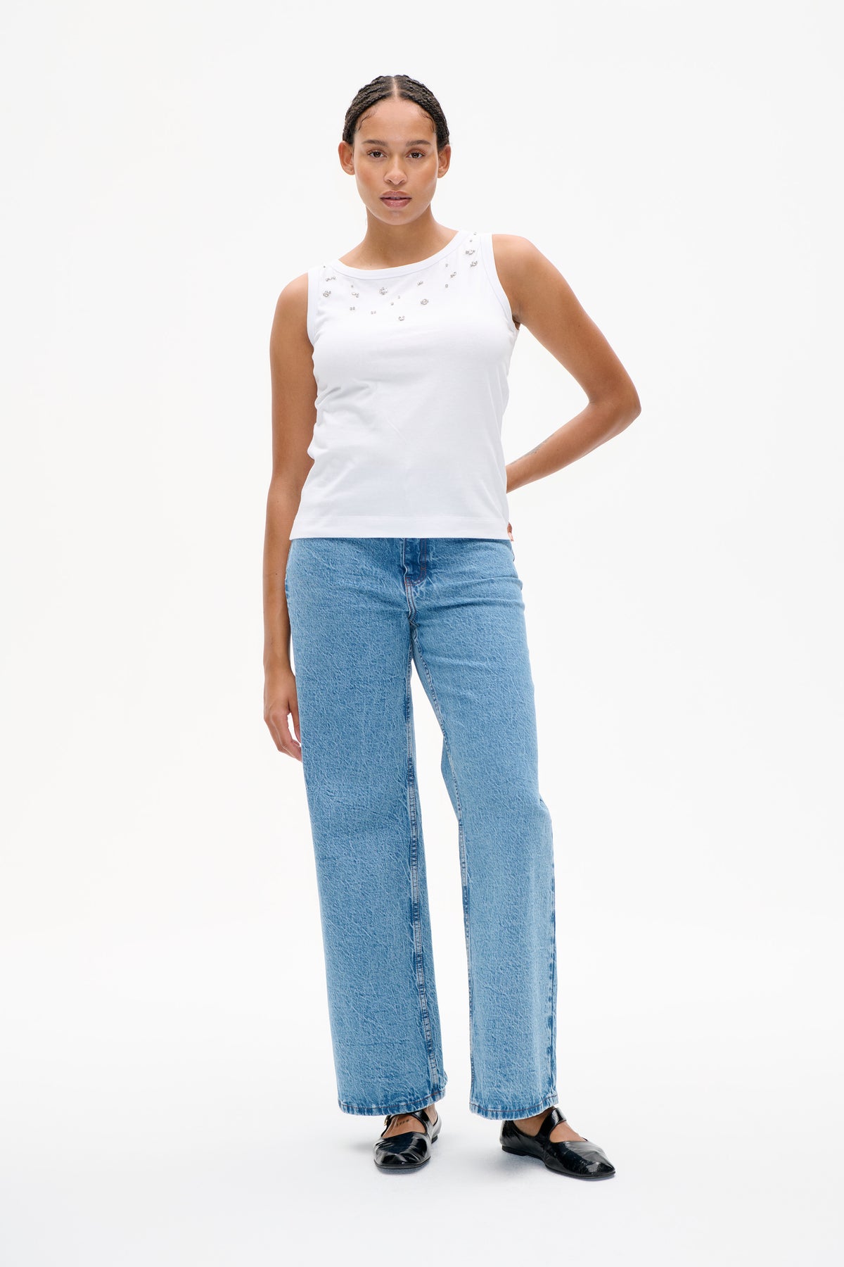 Front view of a white sleeveless top with scattered silver embellishments, styled with wide-leg blue jeans.