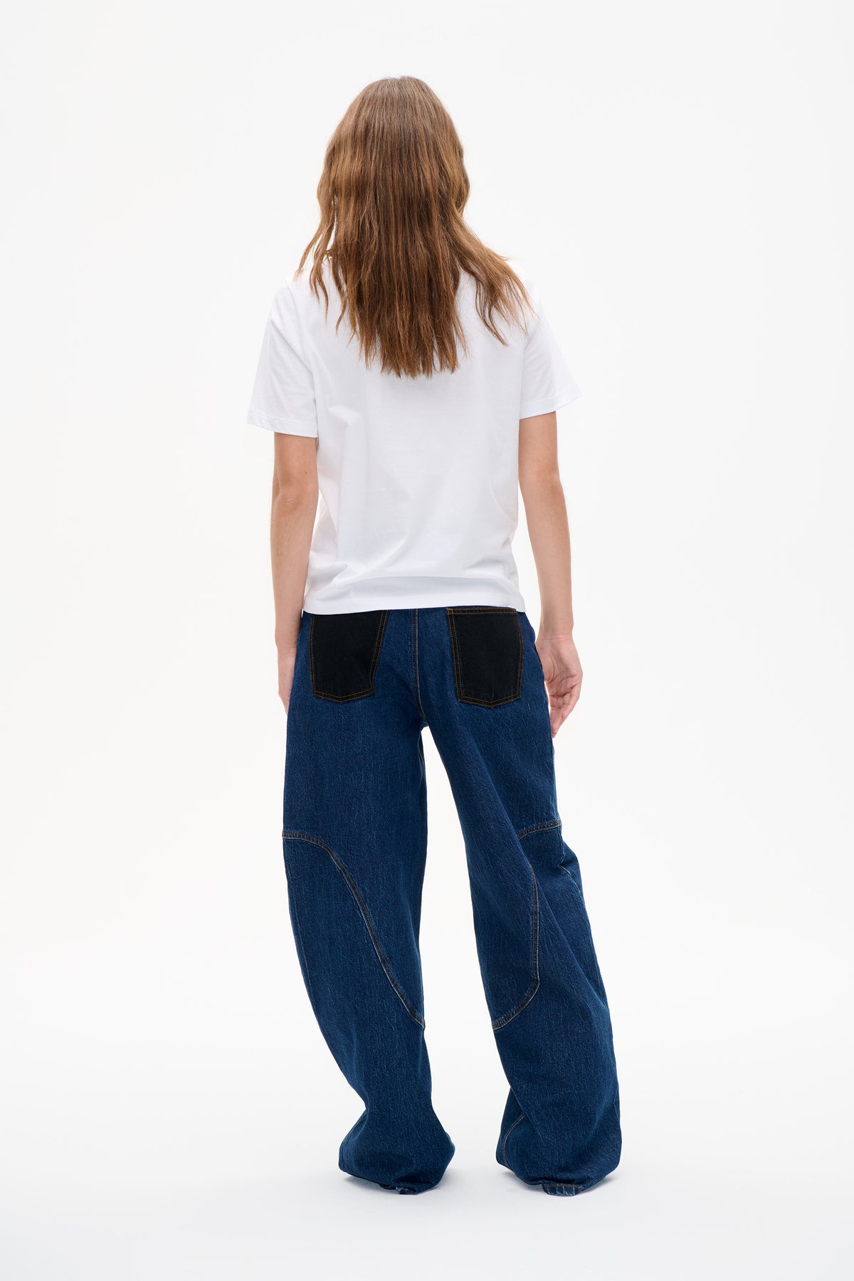 Back view of dark blue wide-leg jeans with black patch pockets and curved contrast-stitched seams, worn with a plain white T-shirt.