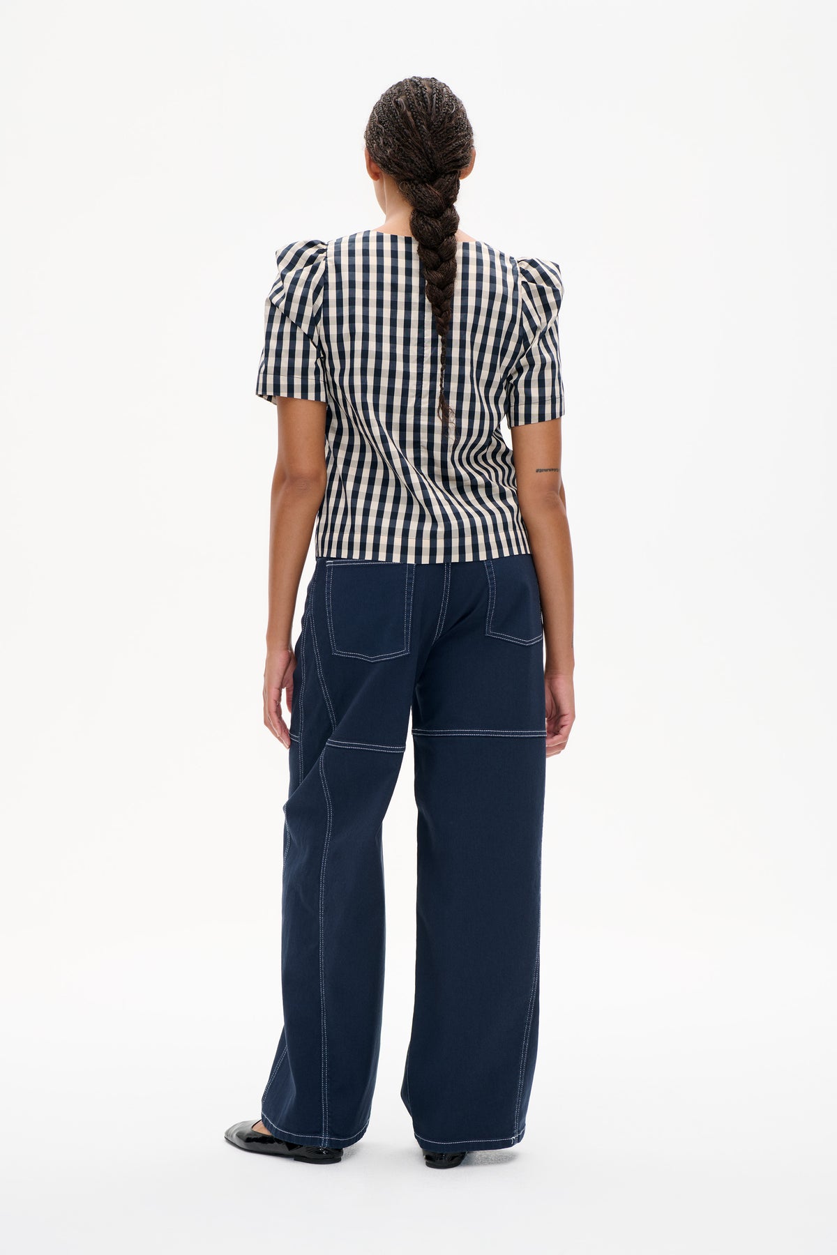 Back view of a model wearing a navy and cream checked short-sleeved top with puffed shoulders and wide-leg navy trousers.