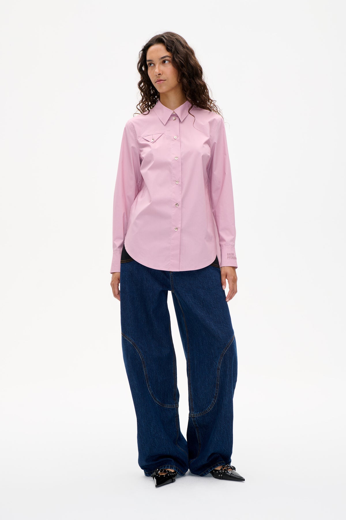Front view of a model wearing a pale pink button-up shirt with a pointed collar and flap chest pocket, paired with dark wide-leg jeans.