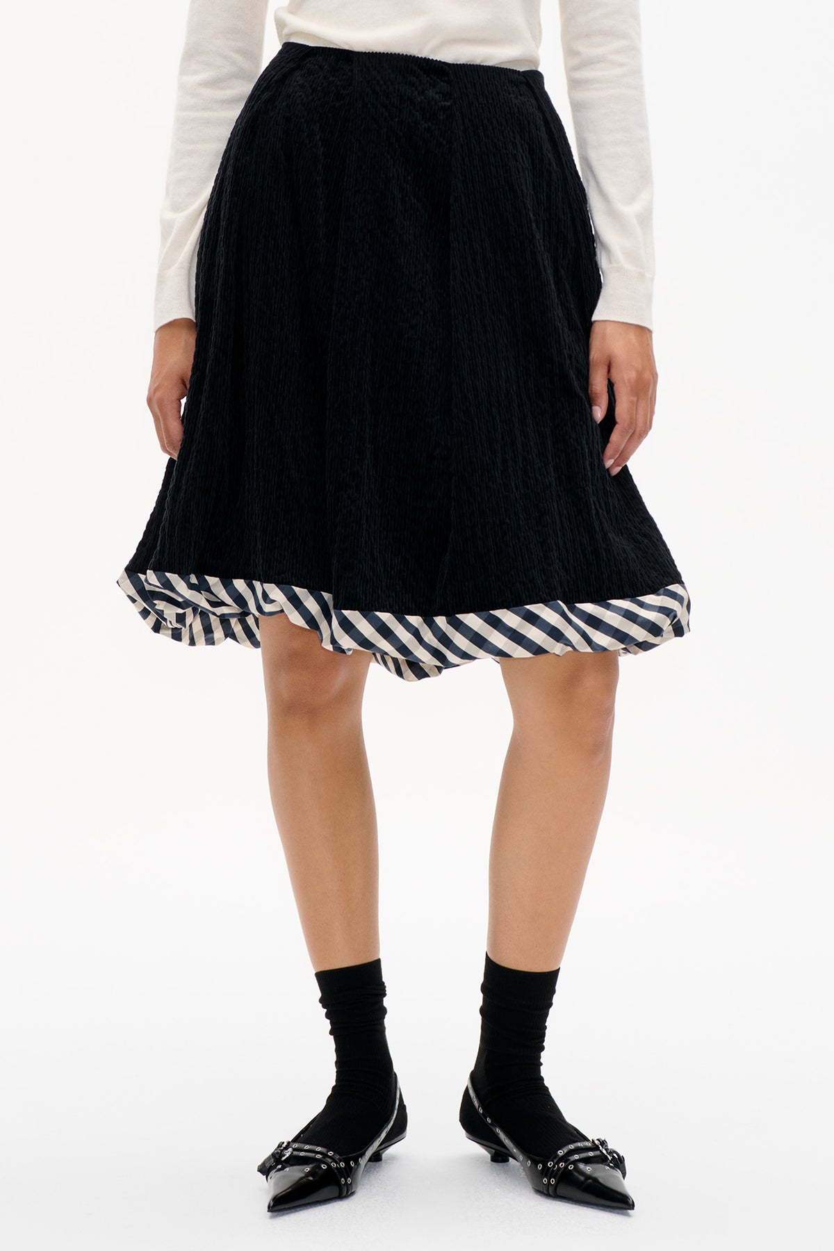 Front detail of a black corduroy A-line skirt with a gathered black-and-white geometric patterned hem.