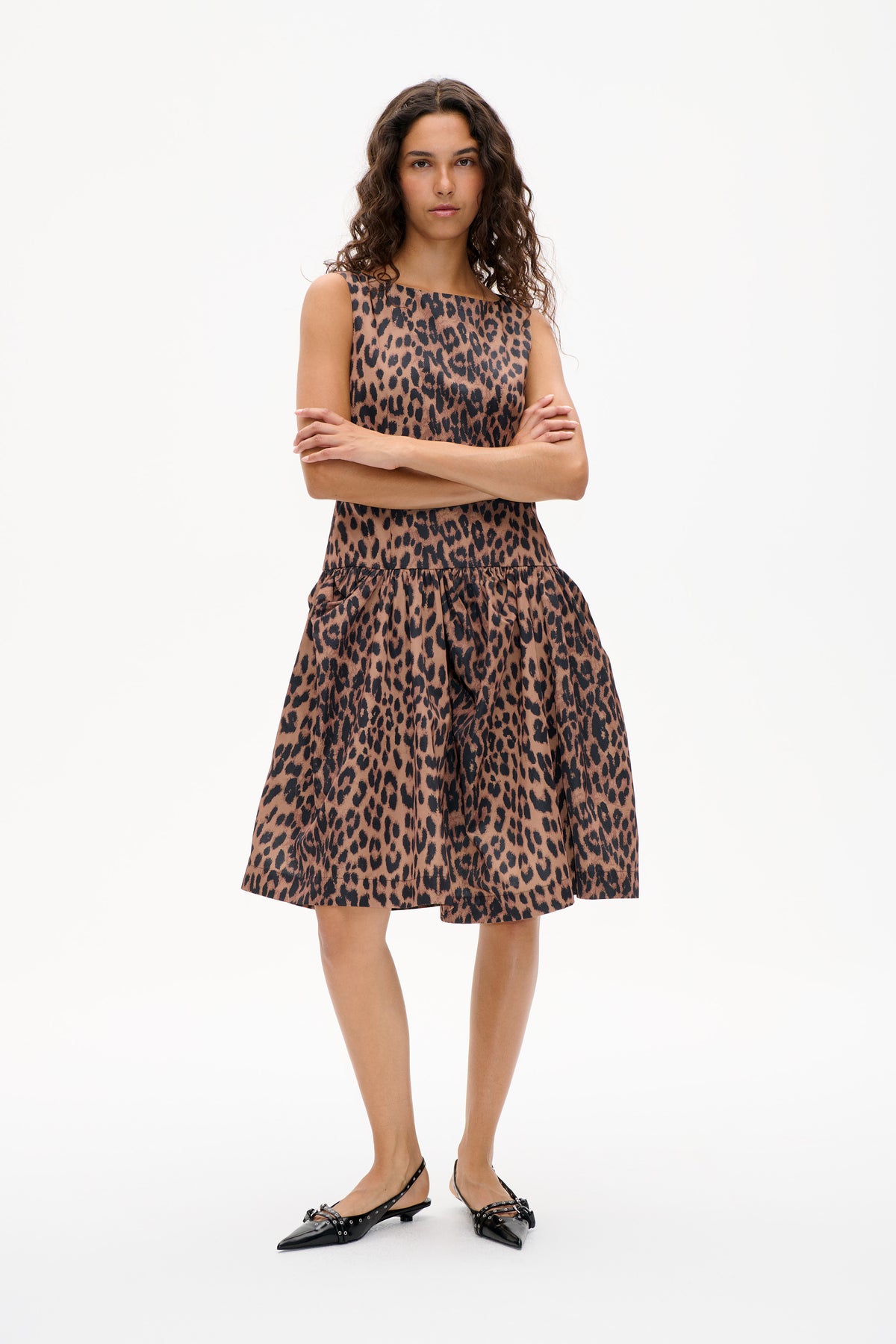 Front view of a sleeveless leopard-print dress in brown and black, with a square neckline and gathered skirt, modeled against a white background.