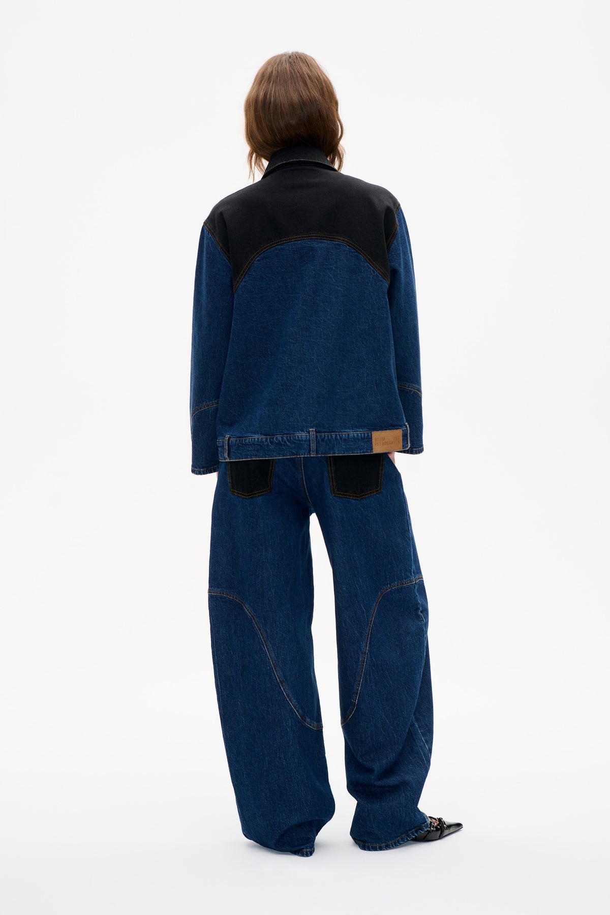 Back view of a model wearing a dark indigo denim jacket with a black shoulder yoke and contrast stitching.