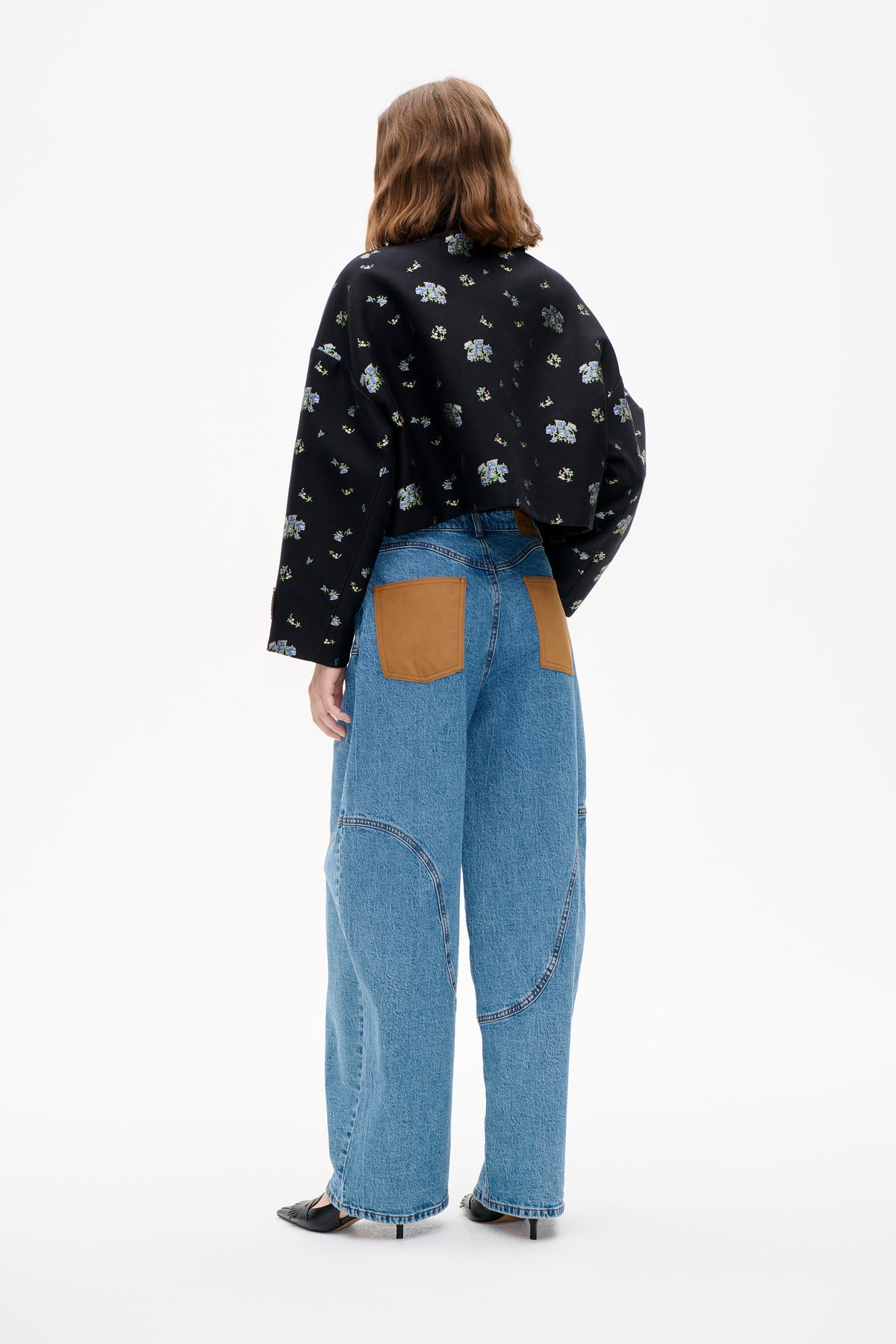 Back view of a black long-sleeved top with scattered blue and green floral print, paired with wide-leg blue jeans featuring tan back pockets.