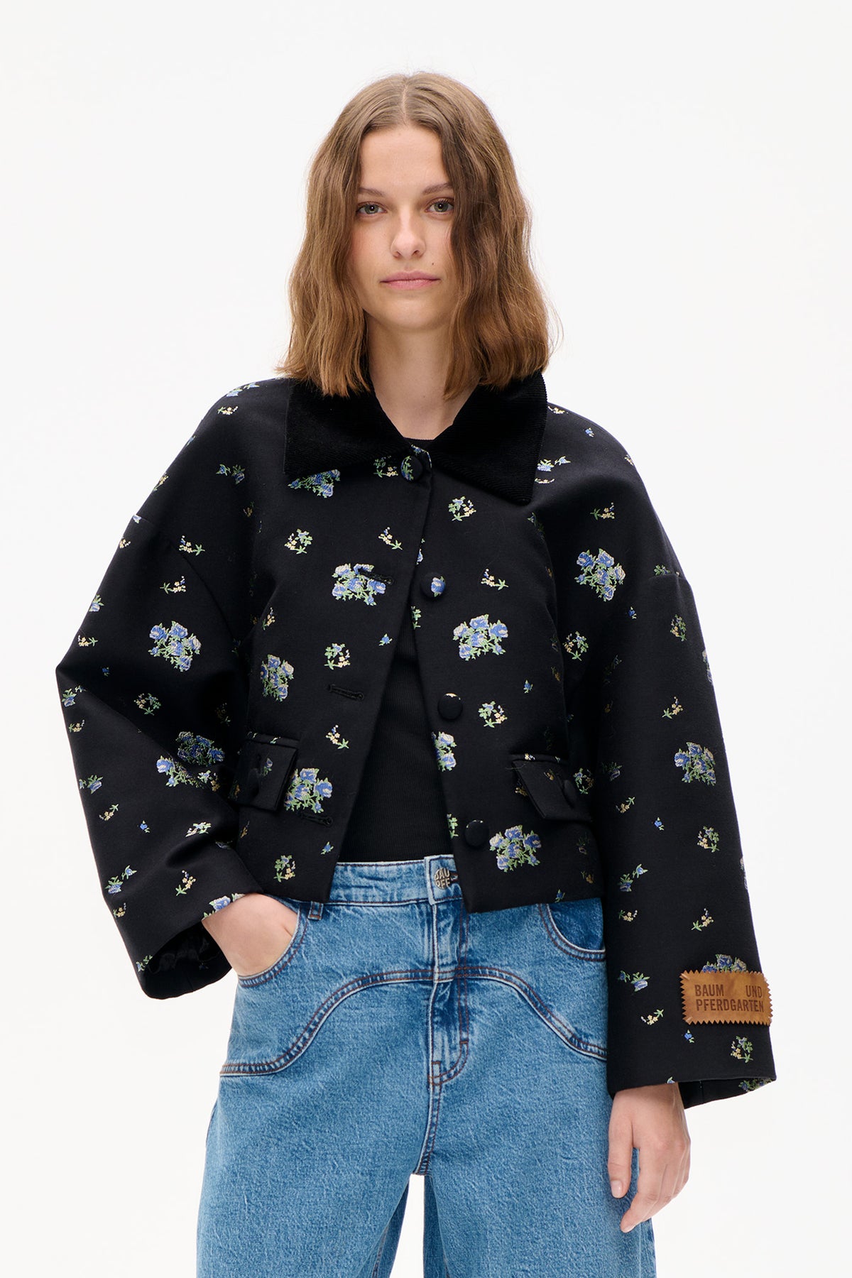 Front view of a black jacket with scattered blue and pale yellow floral print, a wide ribbed collar and covered buttons.