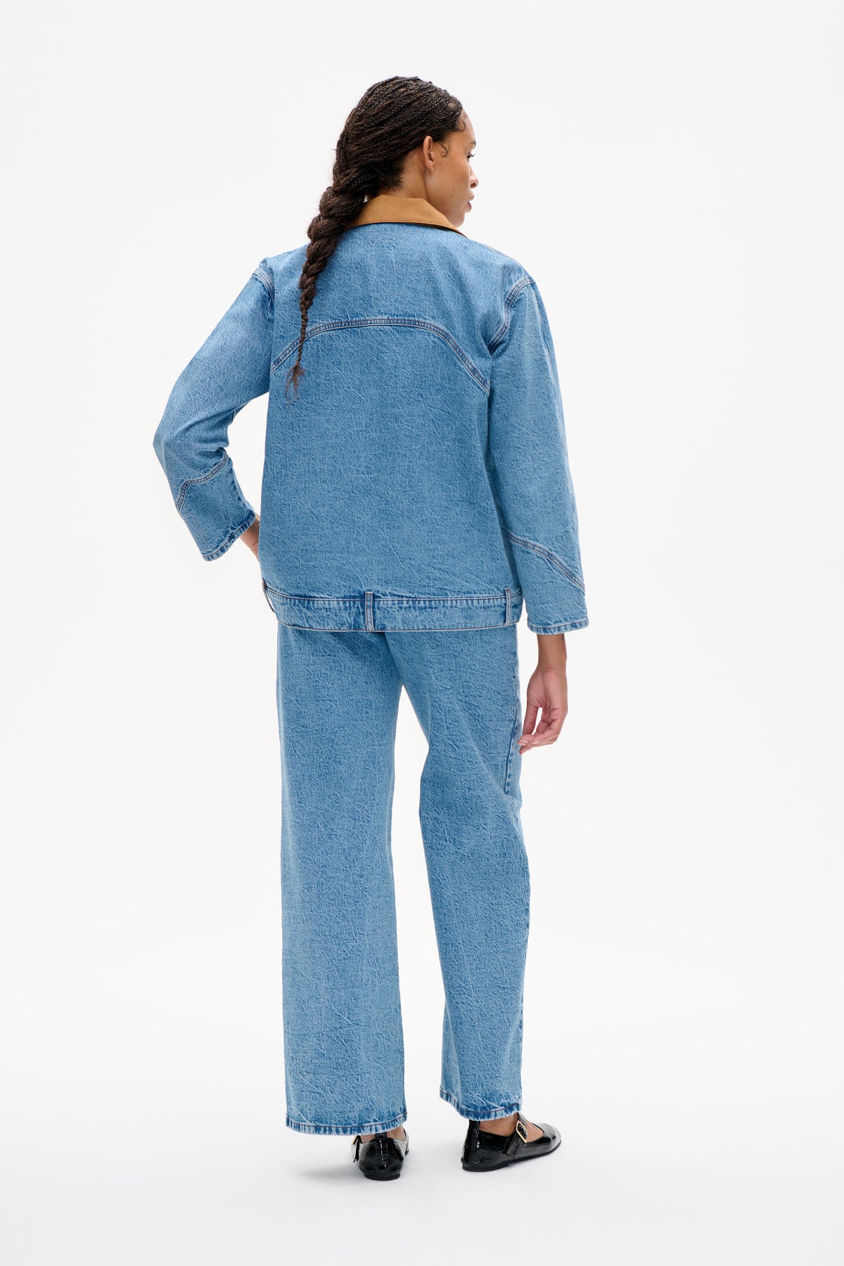 Back view of a model wearing a light blue denim jacket with a tan collar and matching wide-leg jeans.