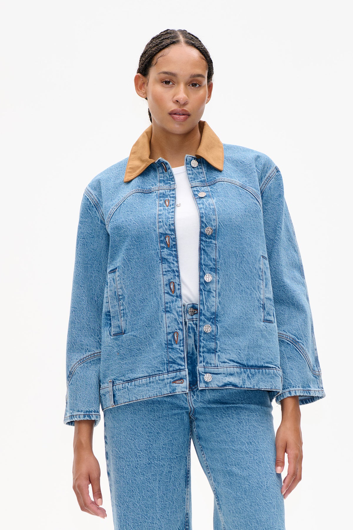Front view of a light-wash denim jacket with a tan contrast collar, button front, curved seams and large patch pockets, styled with matching jeans.