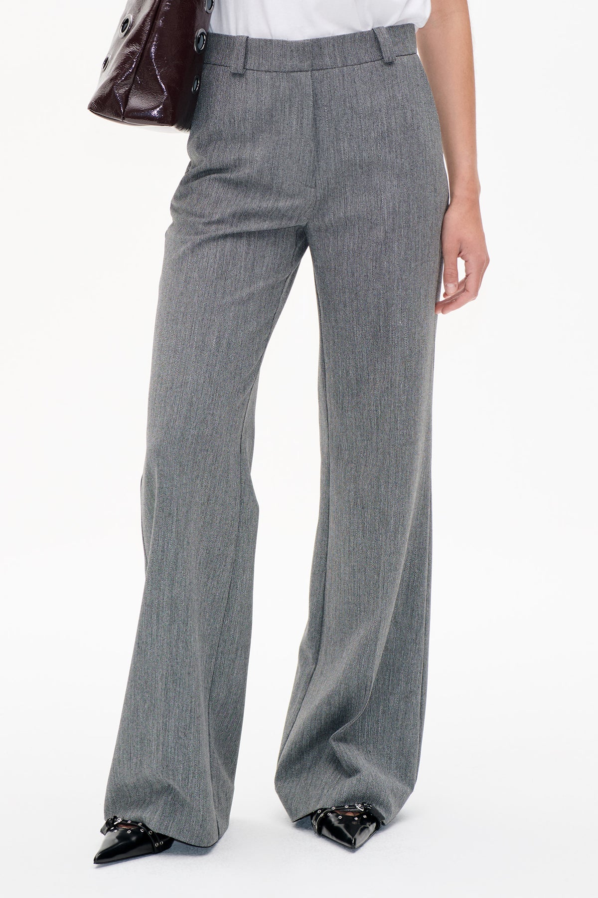 Détail avant rapproché d'un pantalon large gris à taille haute, avec passants de ceinture, plis devant et fine texture verticale.
