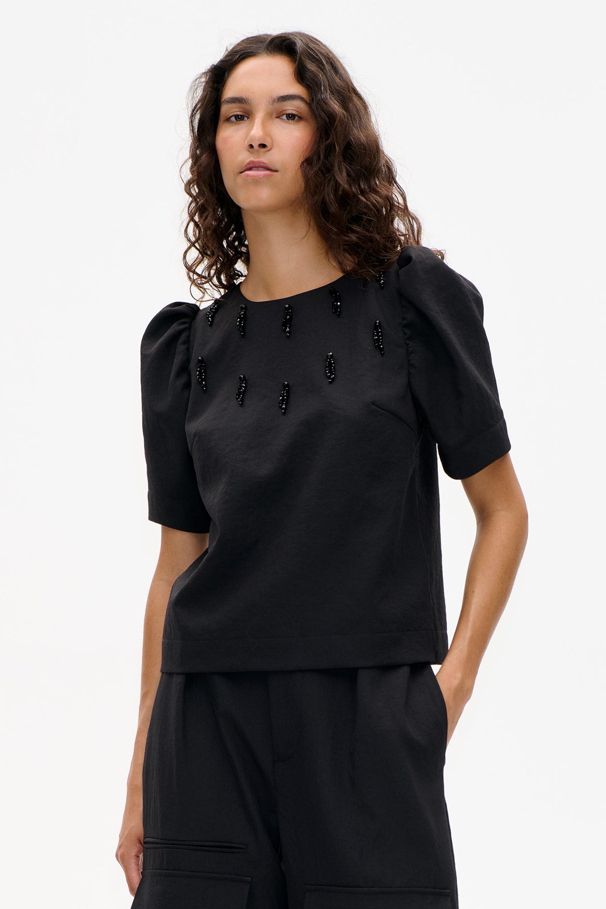 Front view of a black top with puffed short sleeves and scattered black bead embellishments, paired with black trousers.