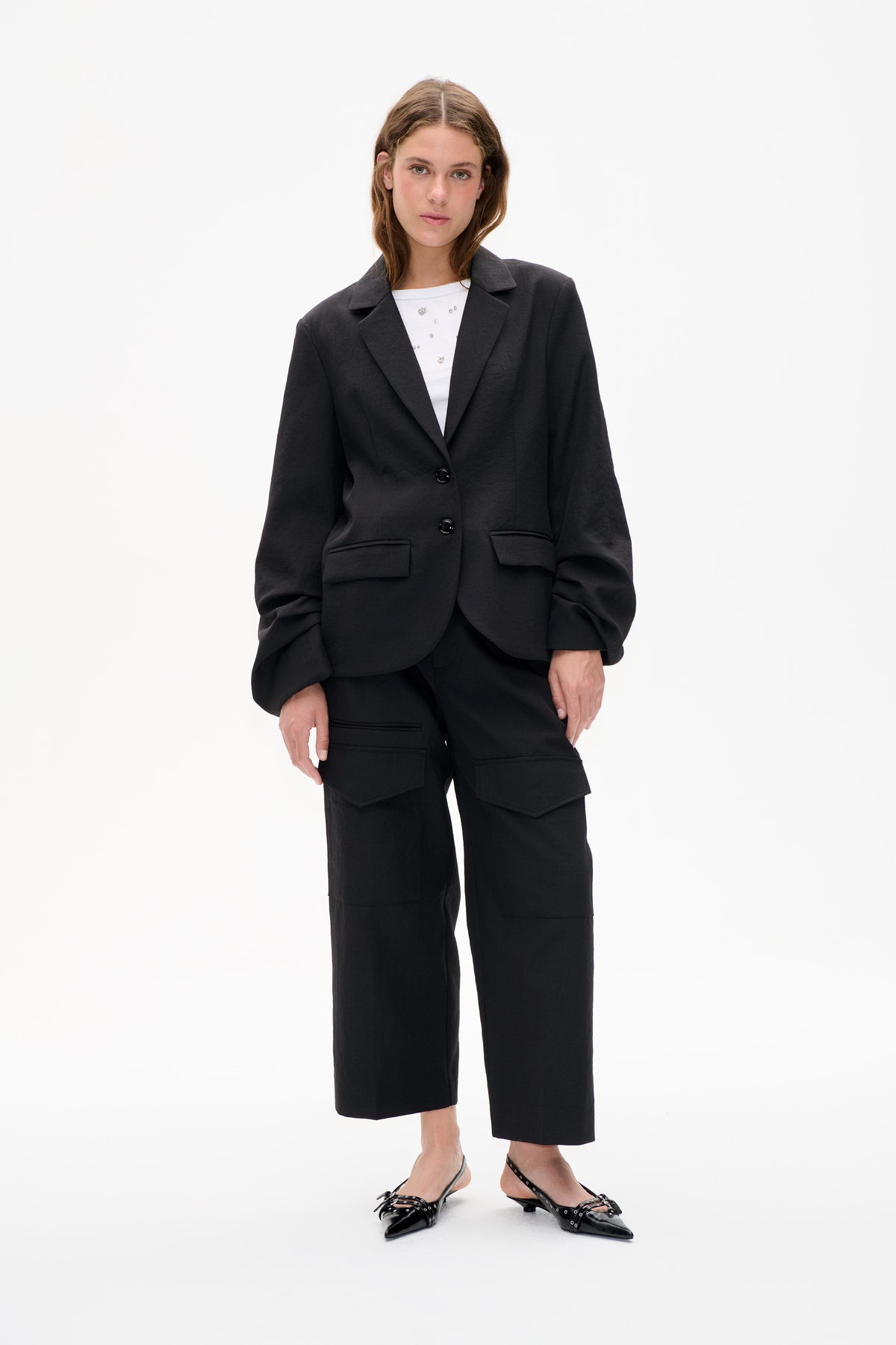 Front view of a model wearing an oversized charcoal blazer with patch pockets, a white embellished top and black wide-leg cropped trousers.
