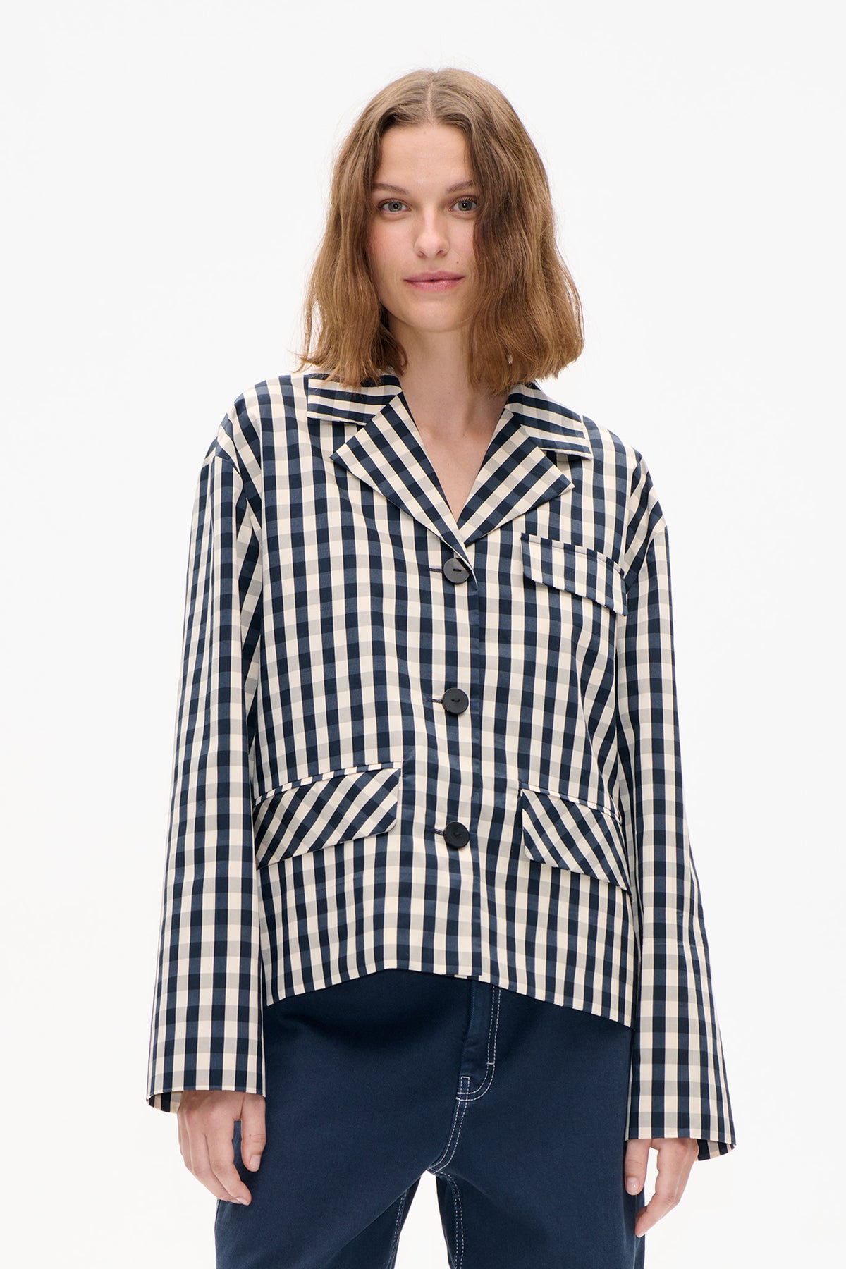 Model wearing a navy and cream checked button-front jacket with a wide collar, long sleeves and flap pockets.