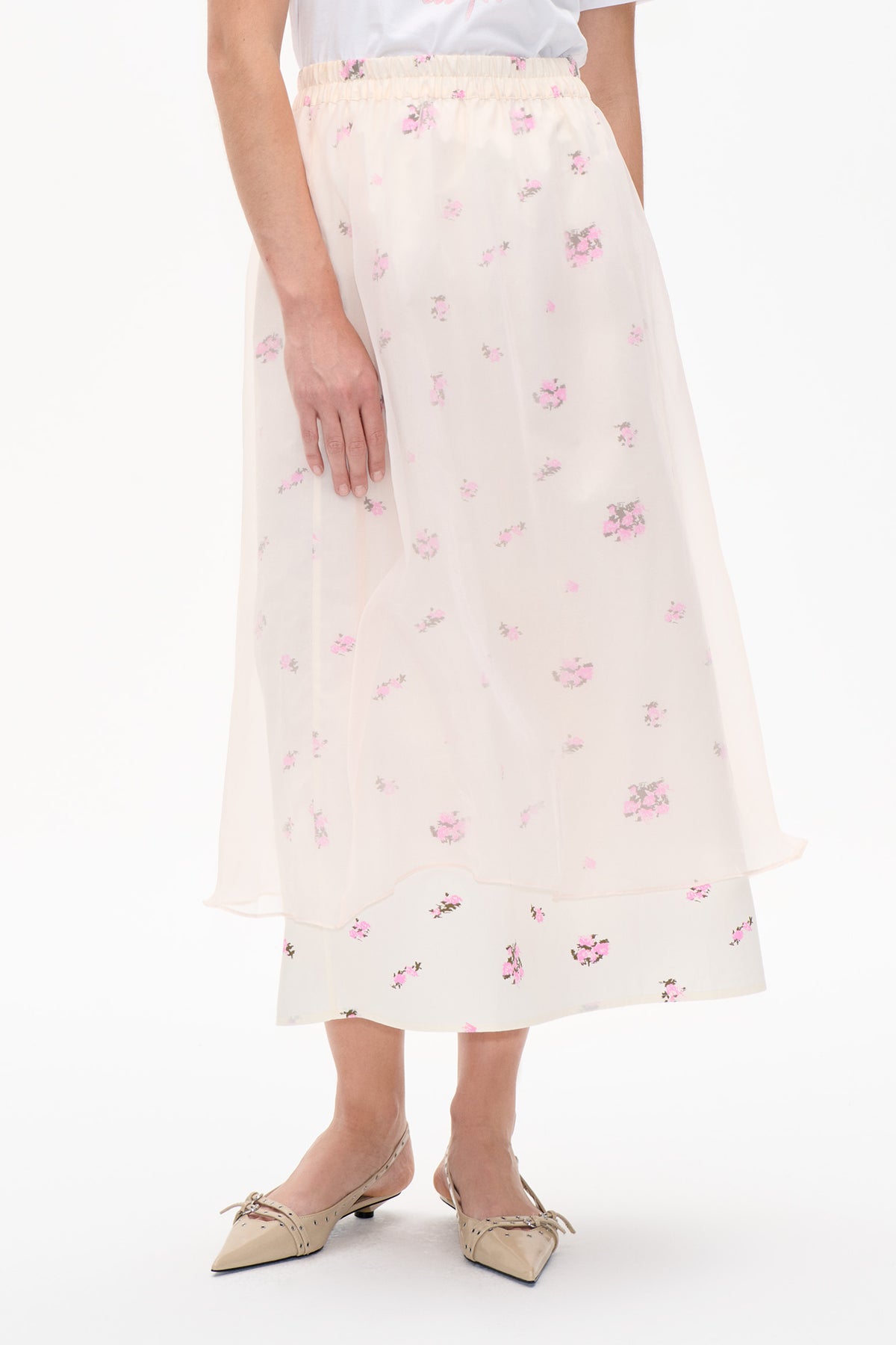 Voordetail van een doorschijnende ivoorkleurige midirok met elastische tailleband en een verspreide roze bloemenprint, gelaagd over een bijpassende rok.