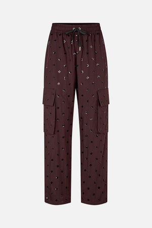 Front view of deep burgundy wide-leg trousers with scattered black and silver flower motifs, an elastic drawstring waist, zip pockets and cargo flap pockets.