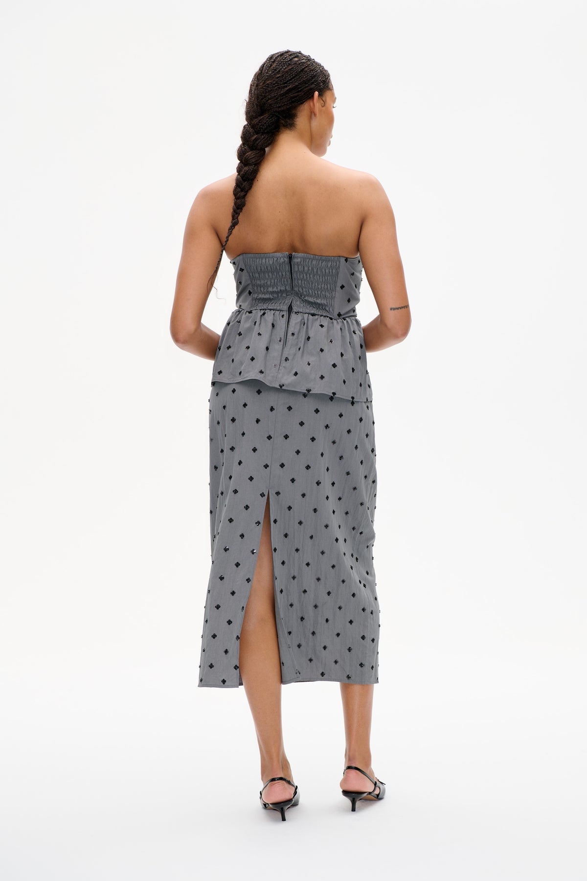 Back view of a strapless grey midi dress with scattered black floral embellishments, a smocked bodice and a high skirt slit.