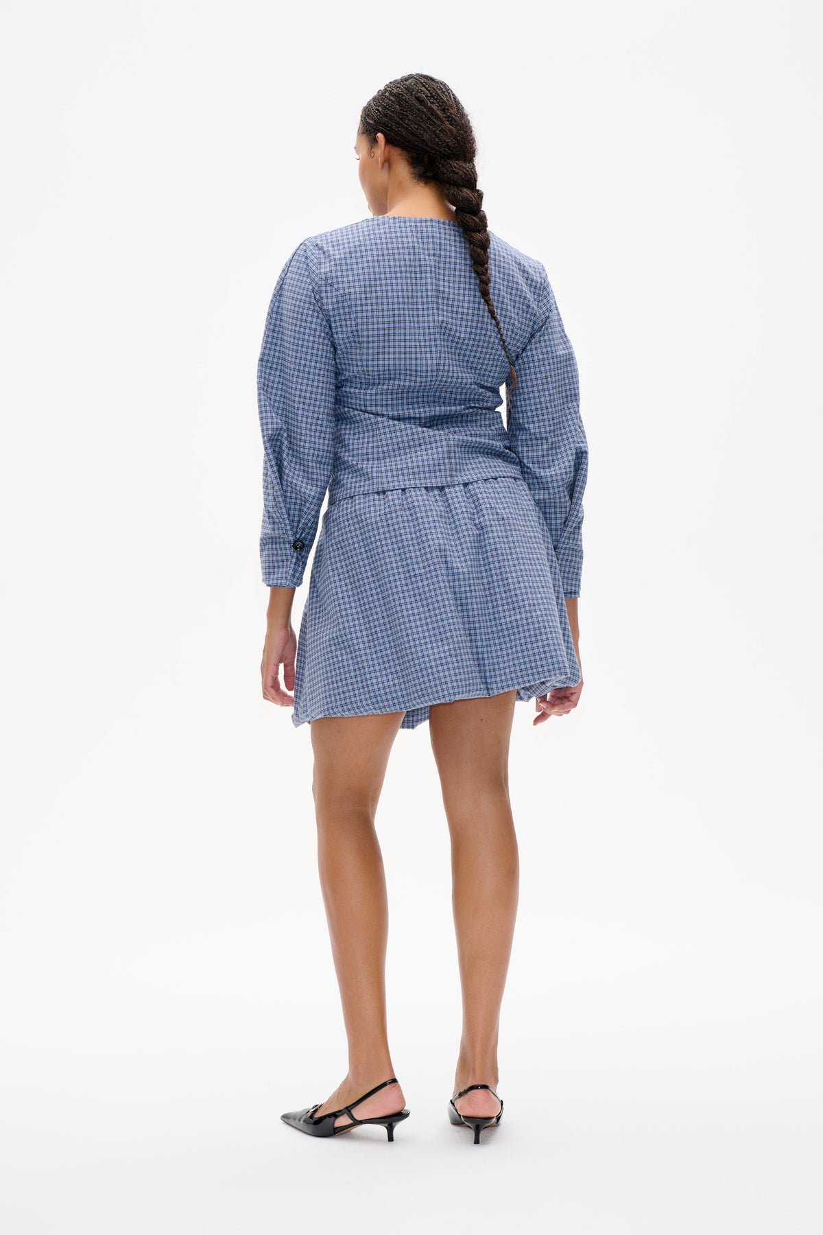 Back view of a model wearing a blue checked long-sleeve top with a gathered waist and matching mini skirt.
