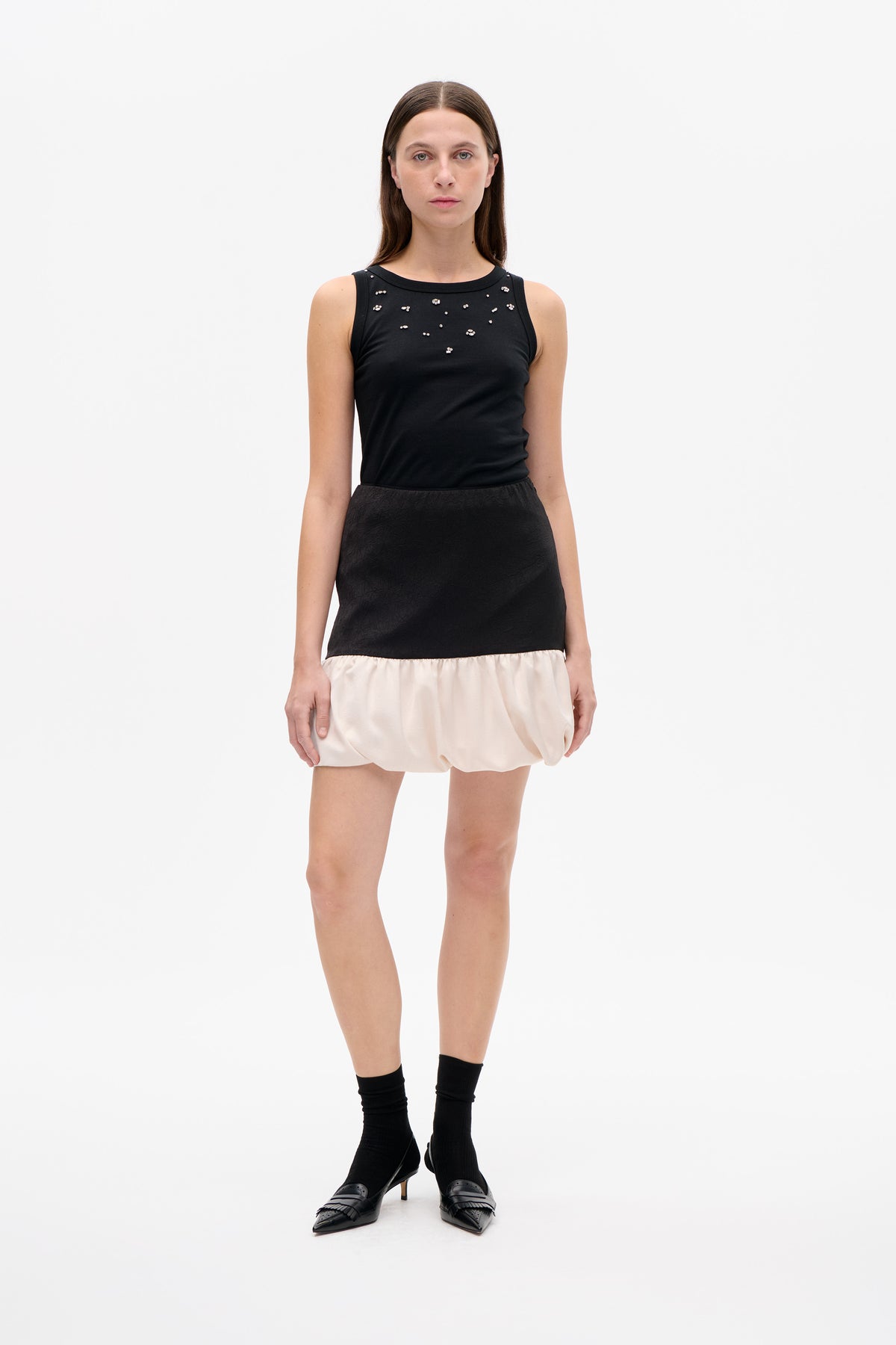 Front view of a black sleeveless dress with scattered sparkling embellishments and a textured black skirt finished with a gathered cream hem.