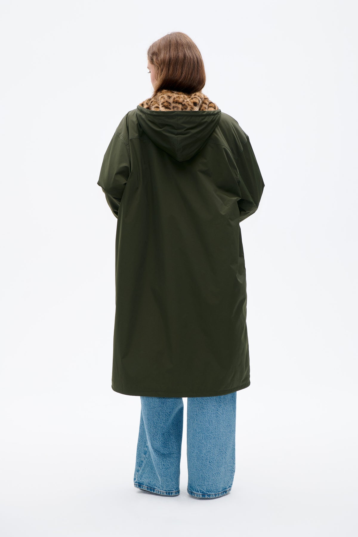 Back view of a long dark olive hooded coat with tan and black leopard-print lining at the collar, styled with blue jeans.