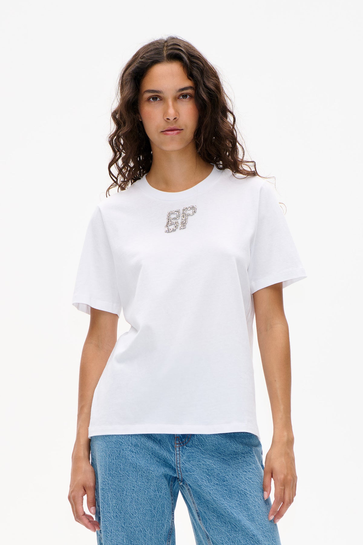 Front view of a model wearing a white short-sleeved T-shirt with a crystal-studded BP emblem and blue jeans.