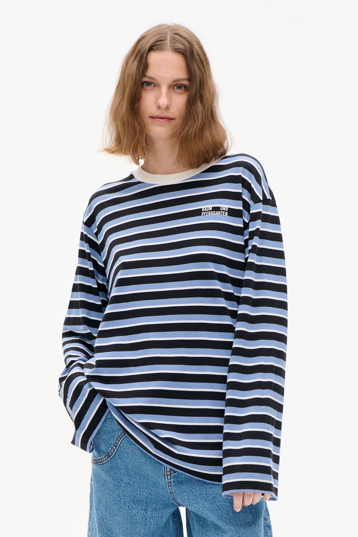 Front view of a model wearing a black, light blue and white striped long-sleeve top with a small chest logo and blue jeans.