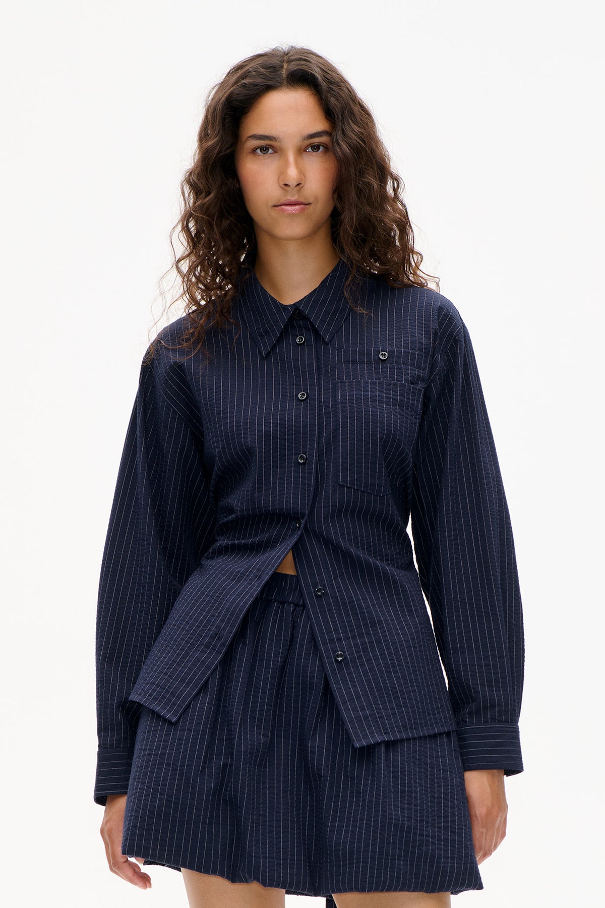 Front view of a navy pinstripe button-front shirt dress with a pointed collar, chest pocket and long sleeves.