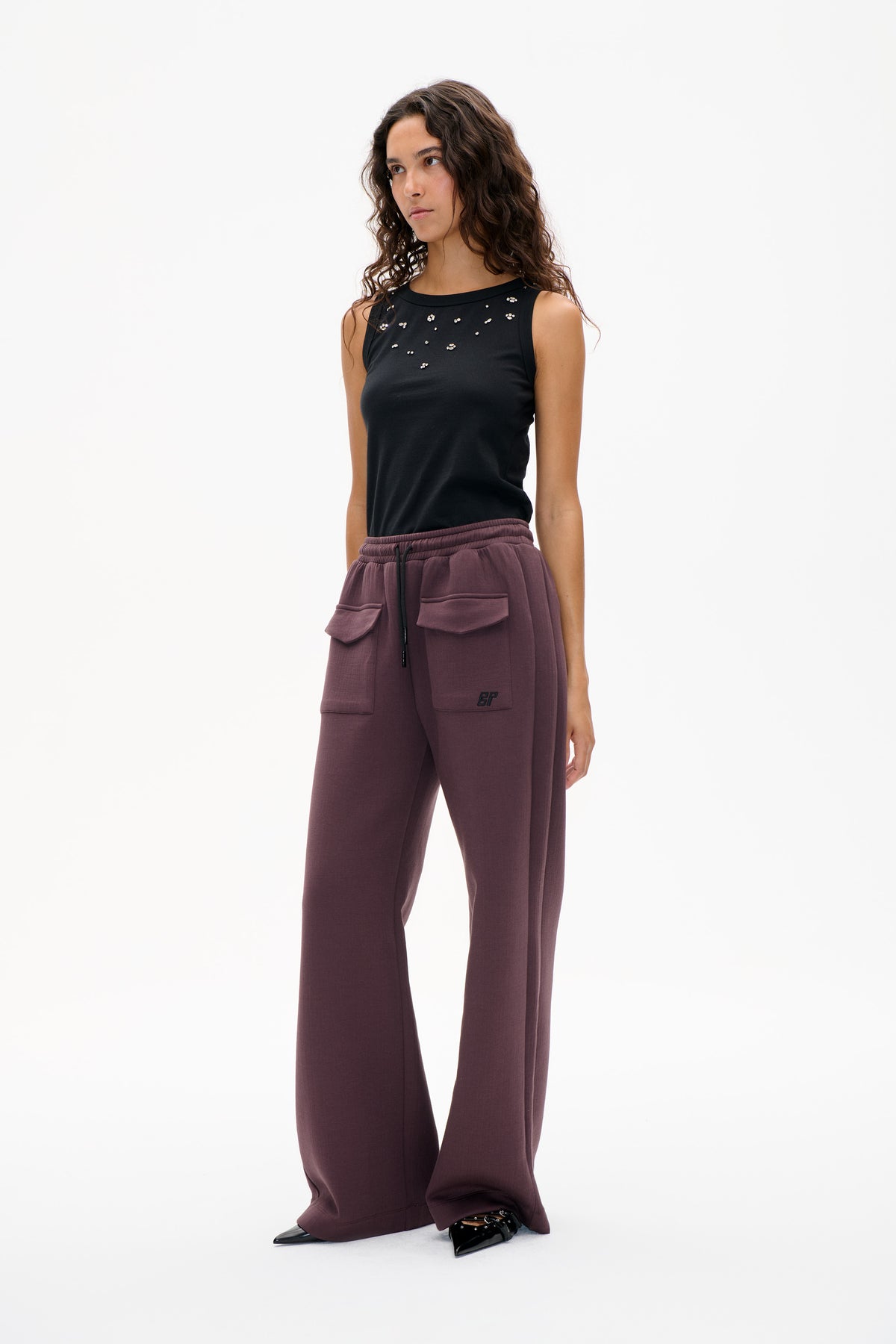 Model wearing a black sleeveless top with scattered silver embellishments and mauve wide-leg trousers with a drawstring waist and patch pockets.