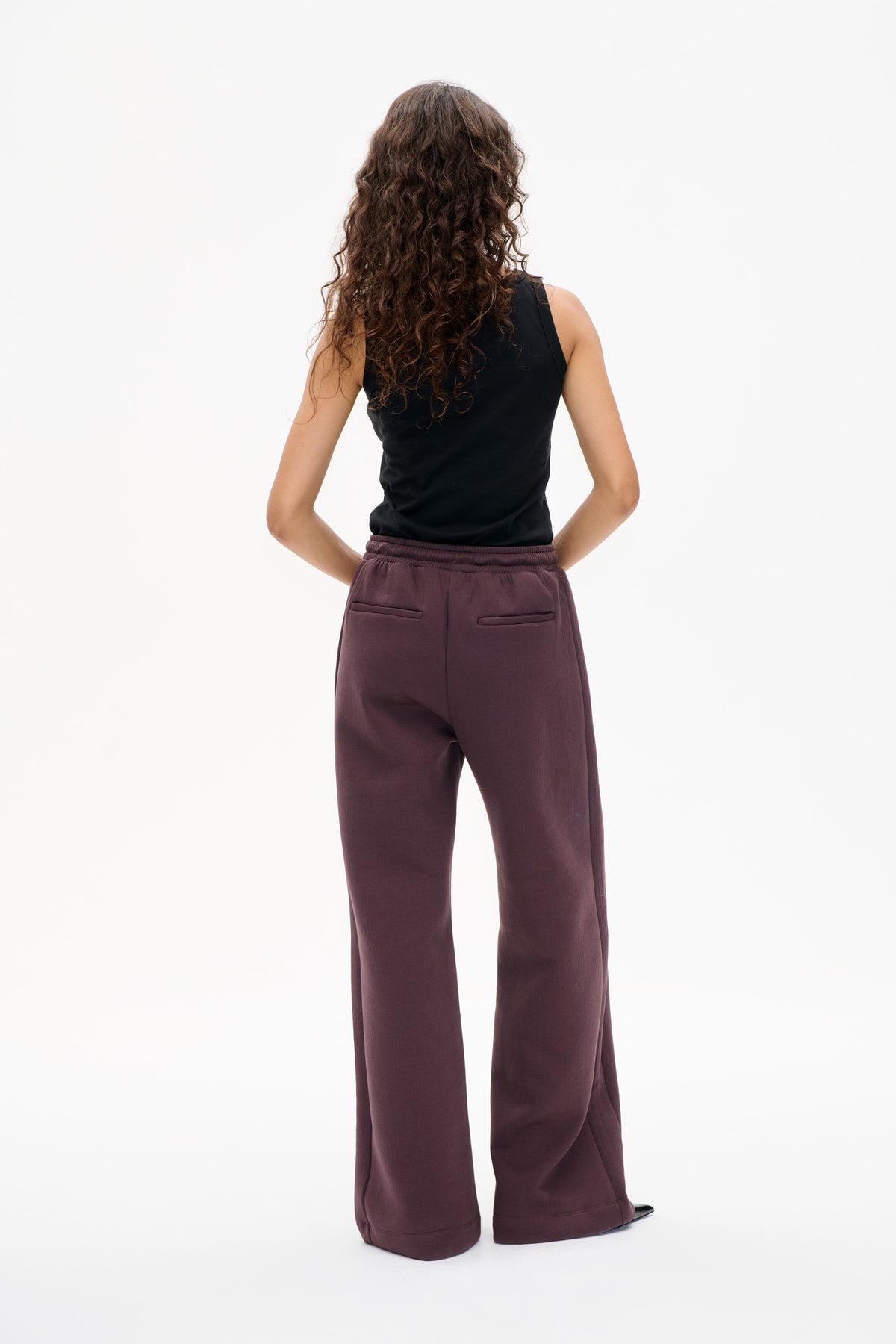 Back view of a black sleeveless top and plum wide-leg trousers with an elasticated waistband and two welt pockets.