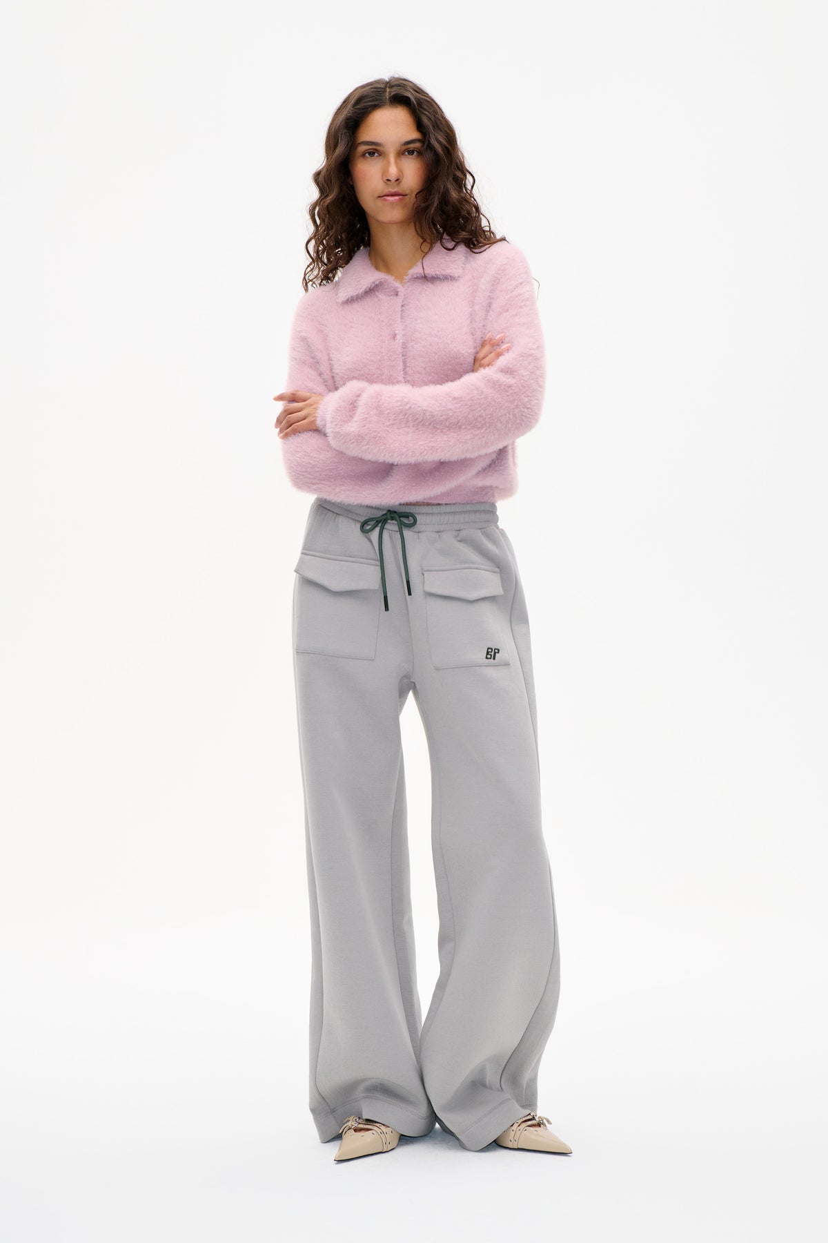Model wearing a fluffy pale pink collared button-front cardigan and grey wide-leg drawstring sweatpants with patch pockets.