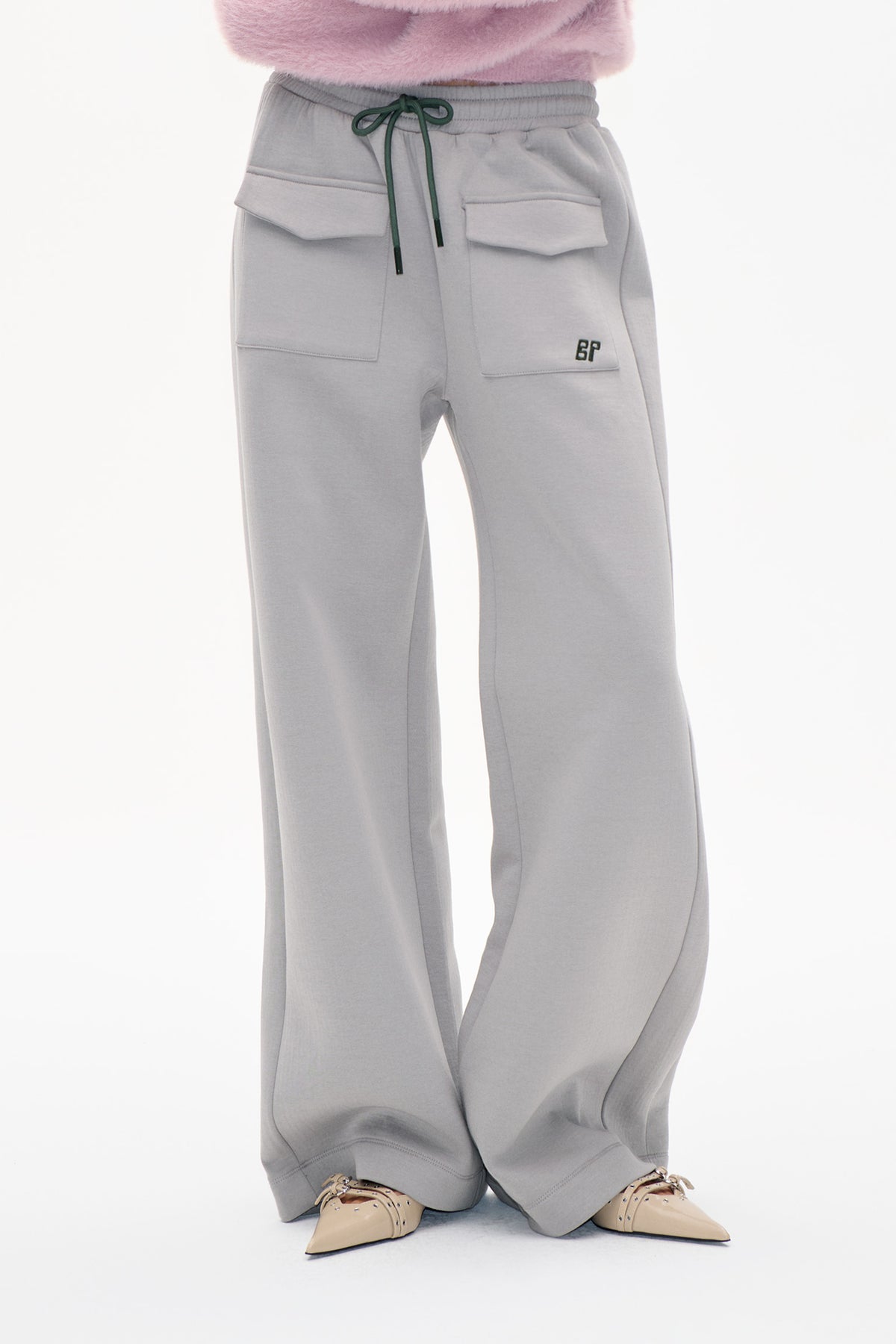Front detail of light grey wide-leg sweatpants with a green drawstring, flap pockets and a small BP logo, worn with a pink fuzzy top.