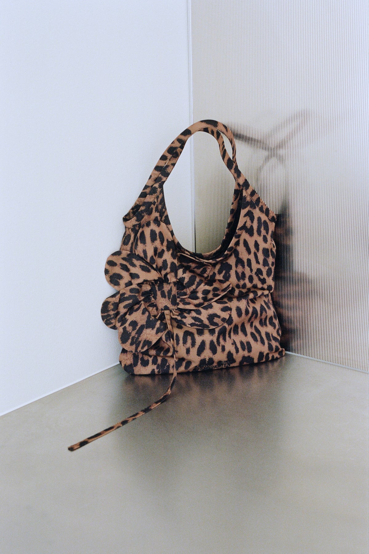 Close-up of a tan and black leopard-print handbag with rounded handles and a long strap resting on the floor