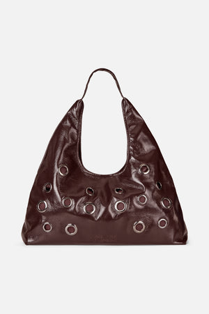 Dark brown glossy slouchy shoulder bag with a single handle and rows of large silver-tone eyelets, shown from the front.