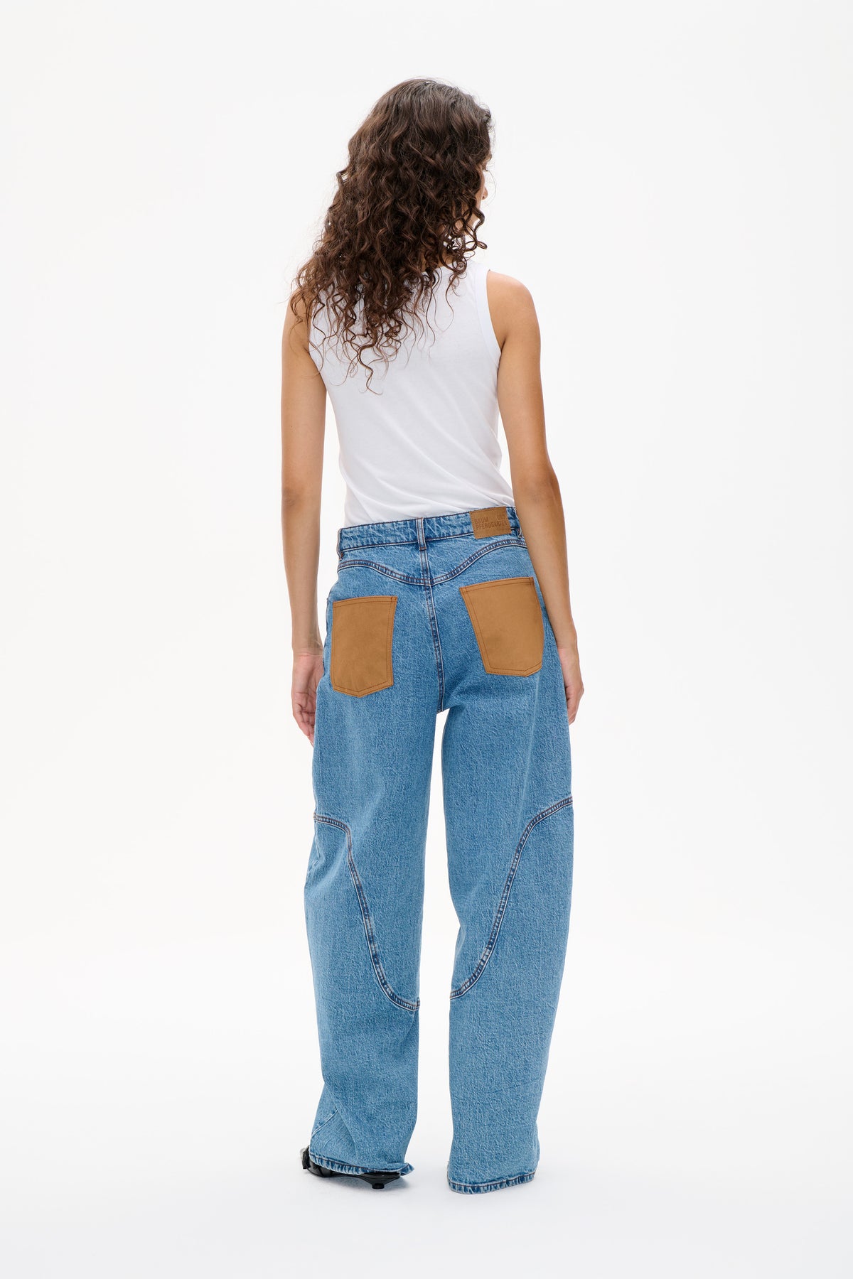 Back view of a white sleeveless top tucked into wide-leg blue jeans with oversized tan patch pockets and curved seams.