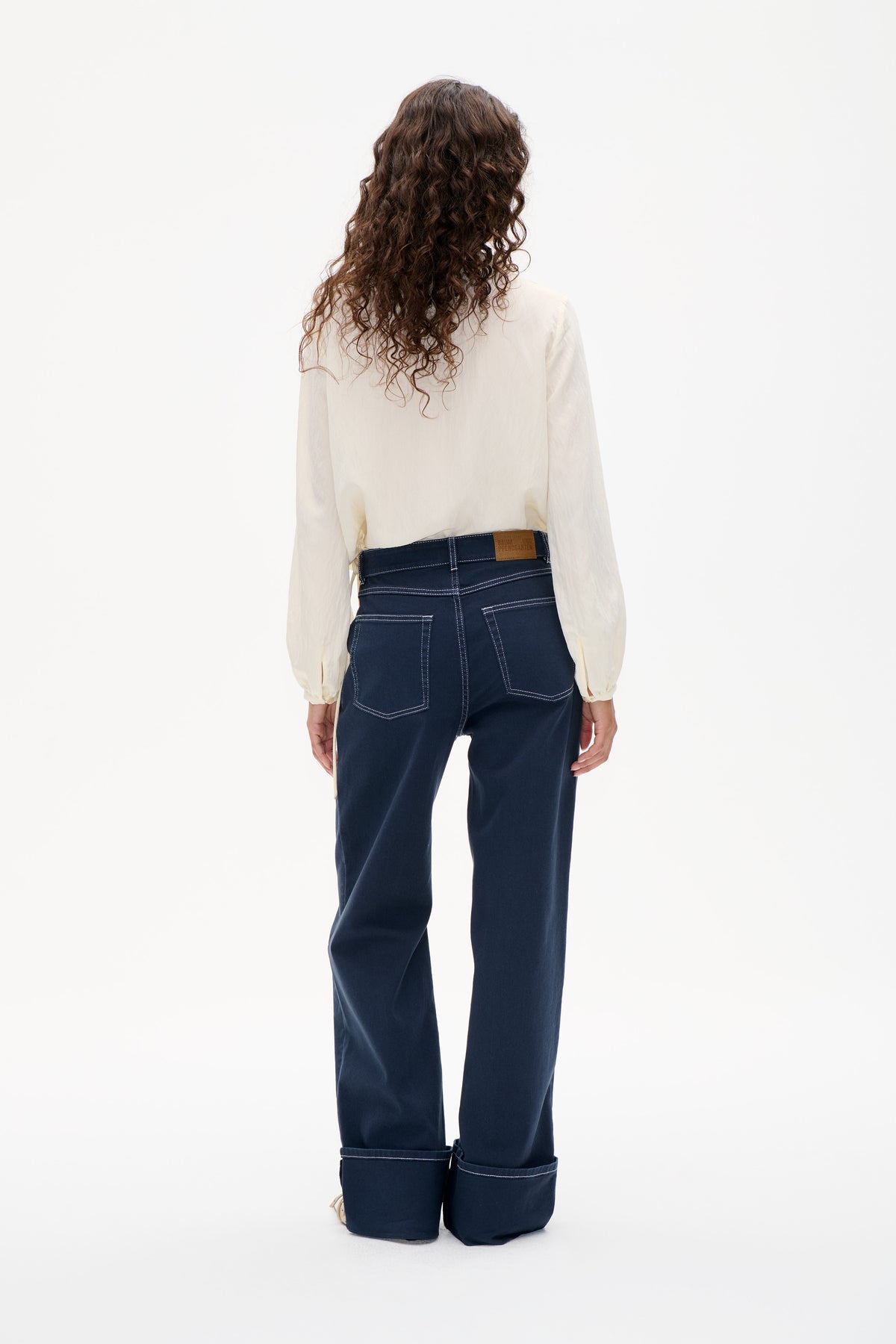 Back view of dark indigo wide-leg jeans with contrast stitching and oversized turned-up cuffs, styled with an ivory long-sleeved blouse.