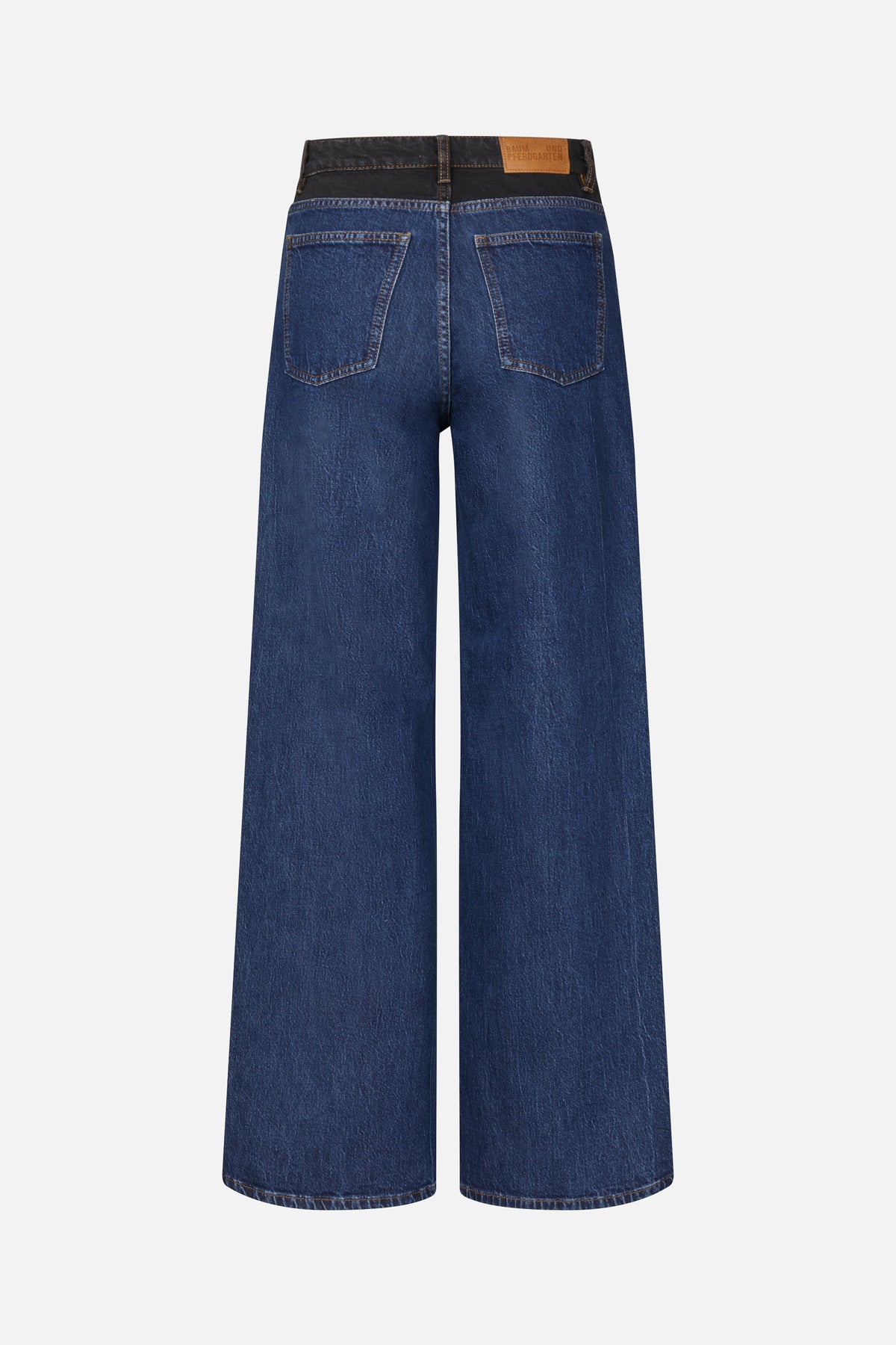 Back view of dark blue wide-leg jeans with contrasting black waistband, tan stitching, two back pockets and a tan logo patch.