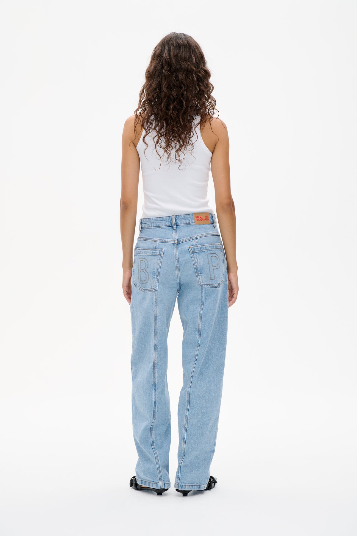 Back view of a model wearing a white sleeveless top and light blue wide-leg jeans with large outlined letter details on the back pockets.