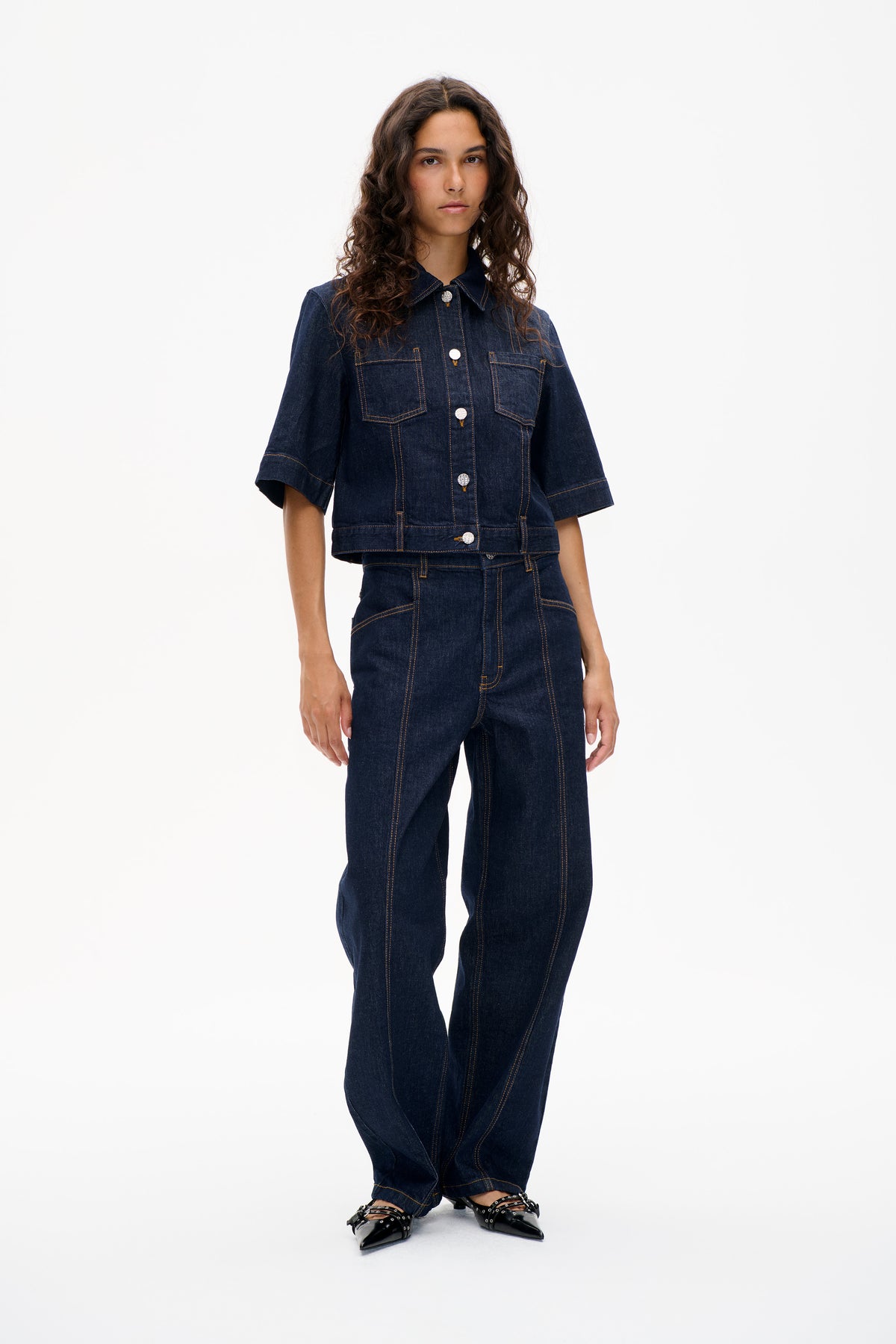 Front view of a model wearing a dark indigo denim jacket with short sleeves and chest pockets, paired with matching wide-leg jeans.