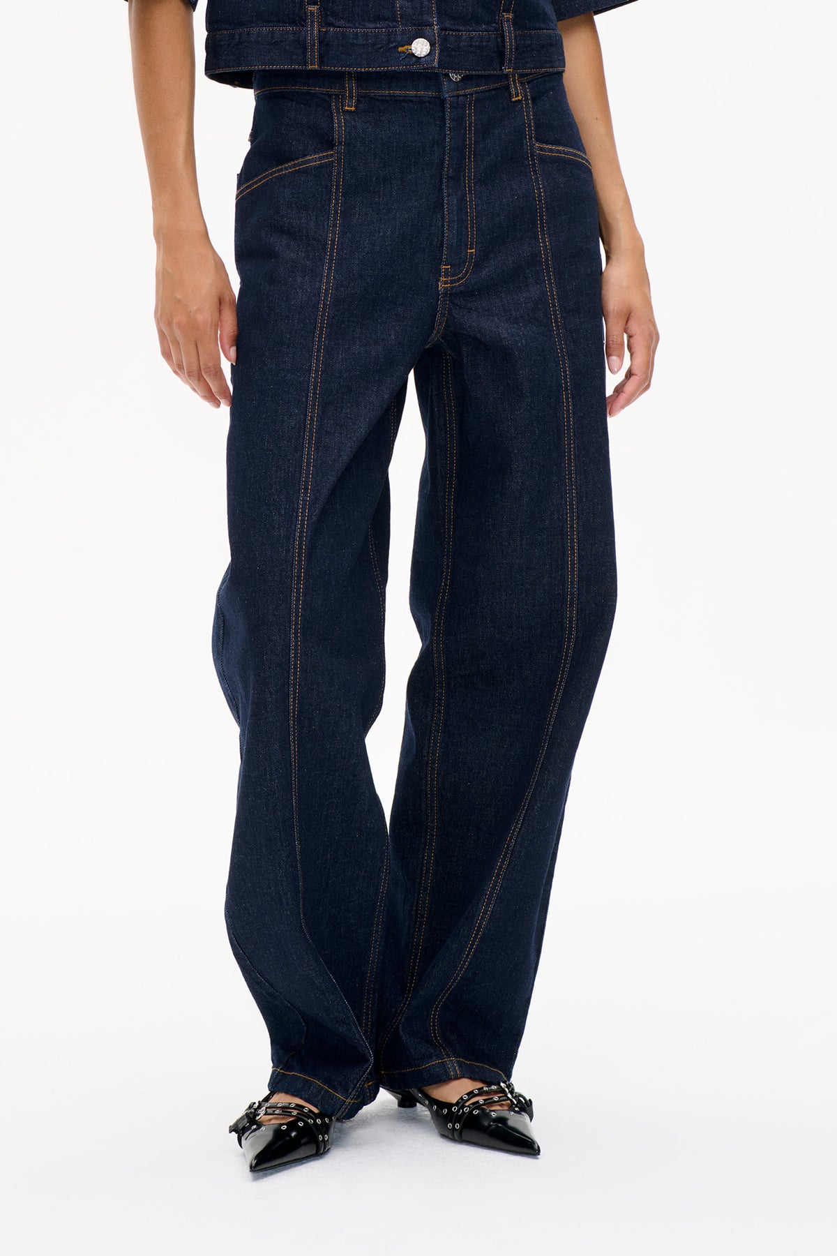 Front detail of dark indigo jeans with curved pockets and prominent orange contrast stitching, styled with a matching cropped denim jacket.