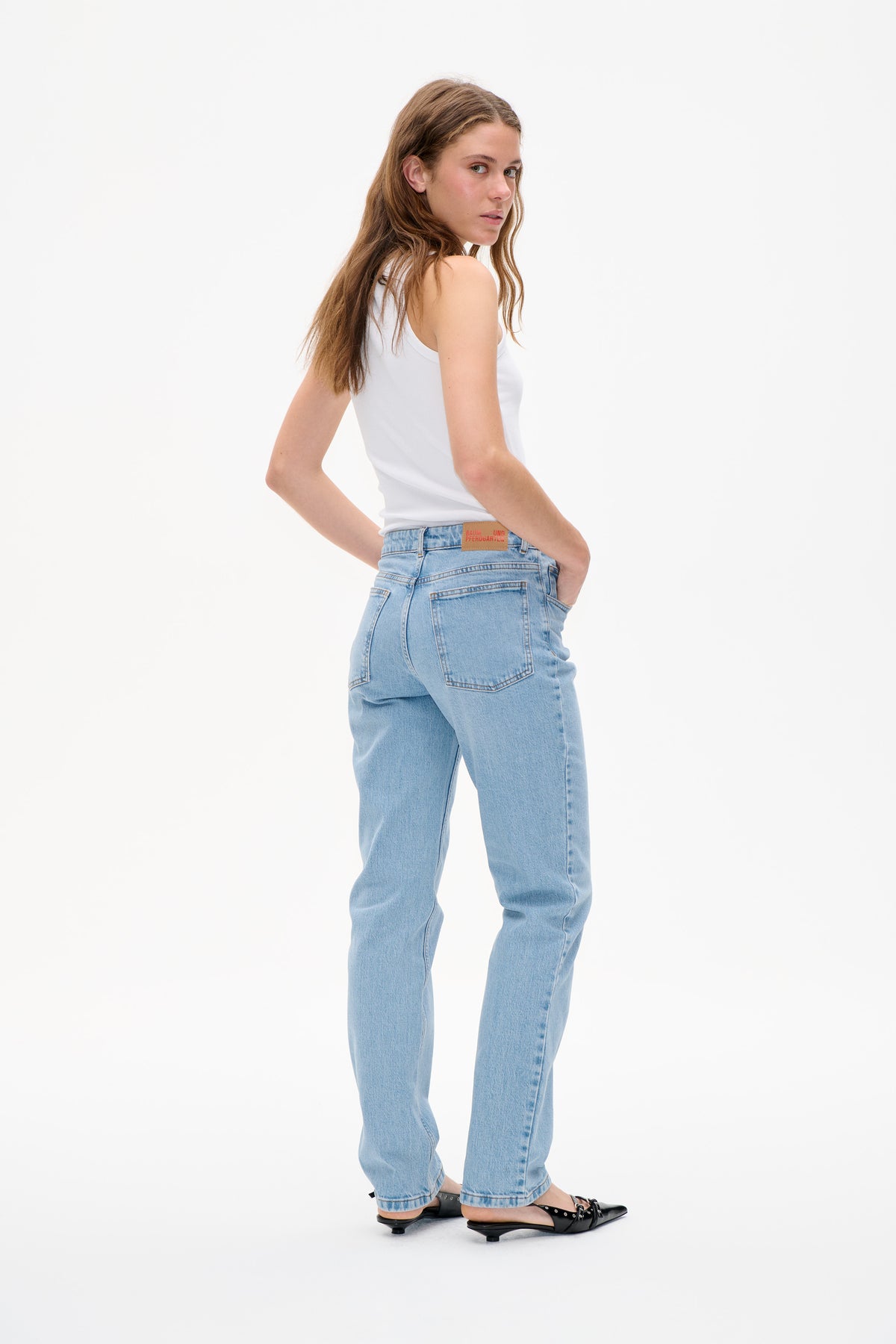 Model wearing a white ribbed tank top and light-wash jeans, shown from the back with patch pockets and a waistband label.
