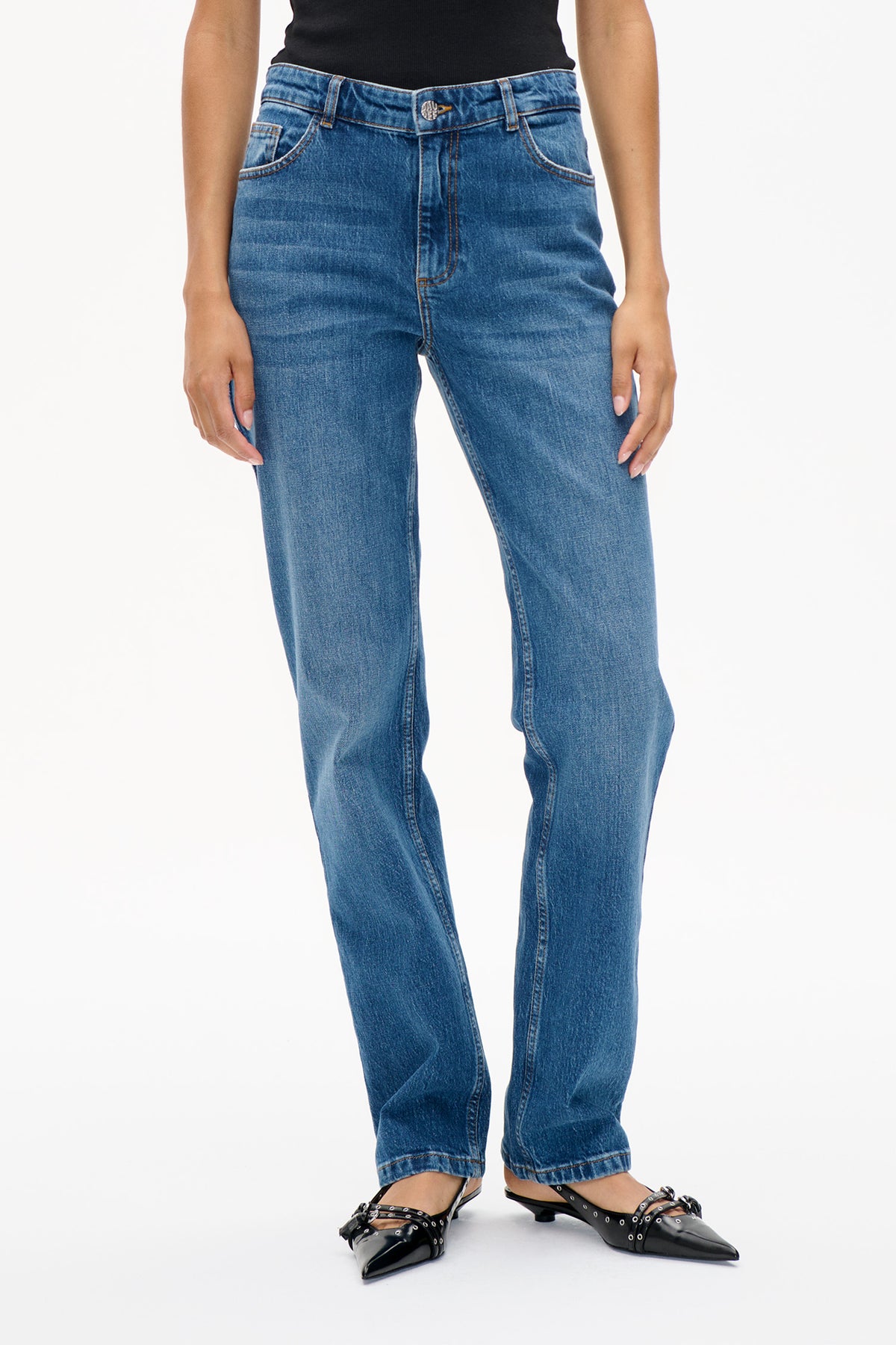 Front detail of blue denim jeans with faded whiskering, contrast stitching, belt loops and a branded metal button, styled with a black top.