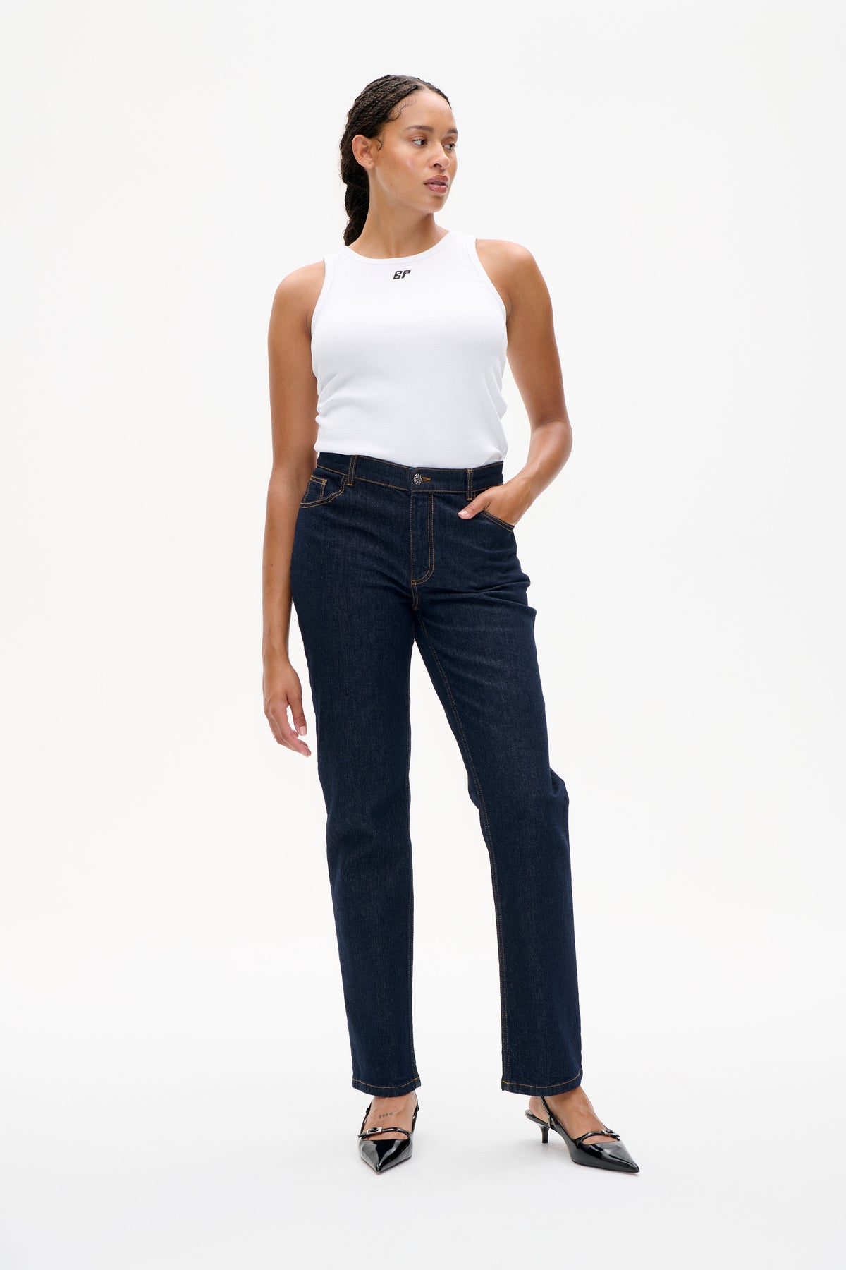Model wearing a white sleeveless ribbed top with a small chest logo and dark indigo straight-leg jeans, shown from the front.