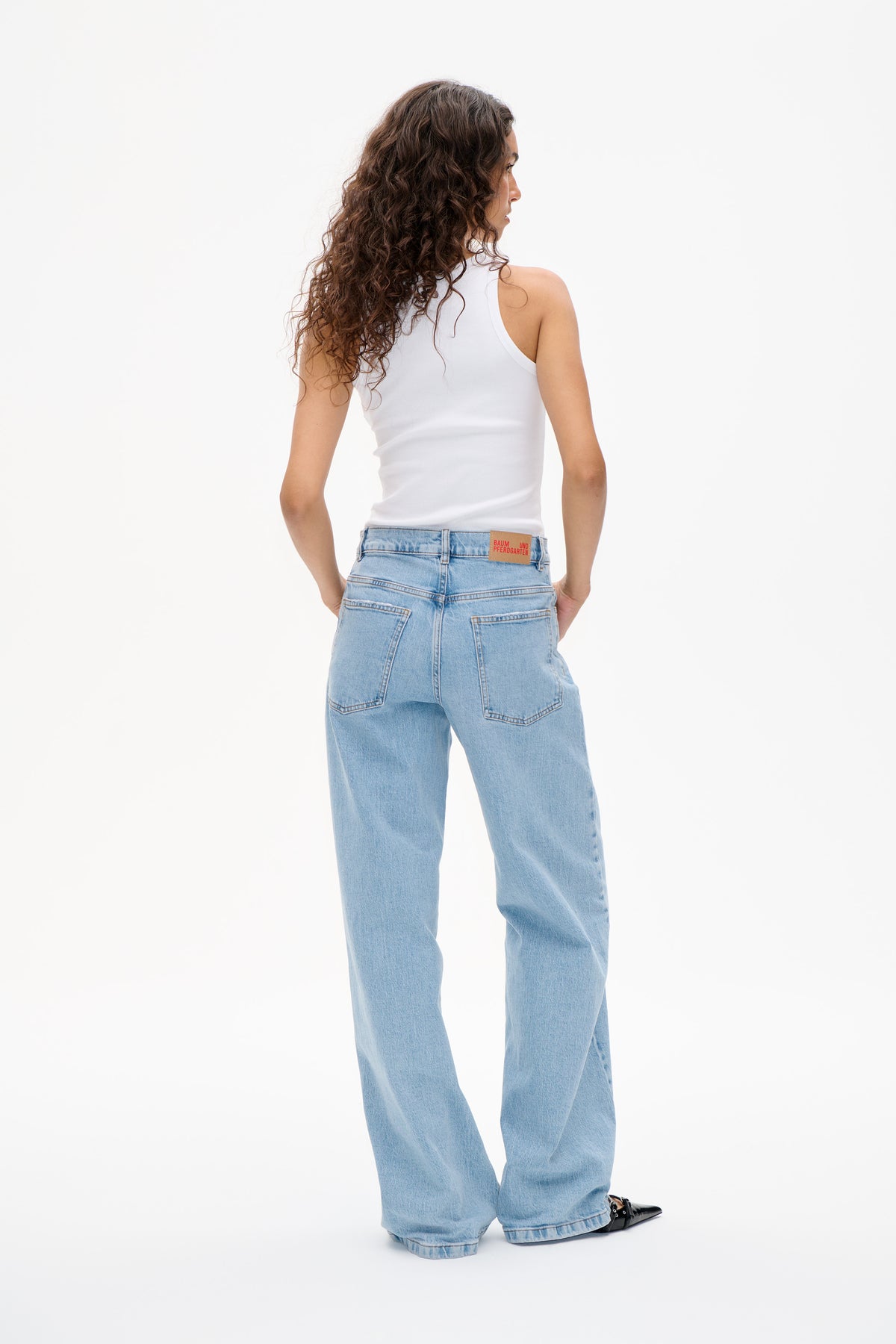 Rear view of a model wearing light blue wide-leg jeans with back patch pockets and a white sleeveless ribbed top.