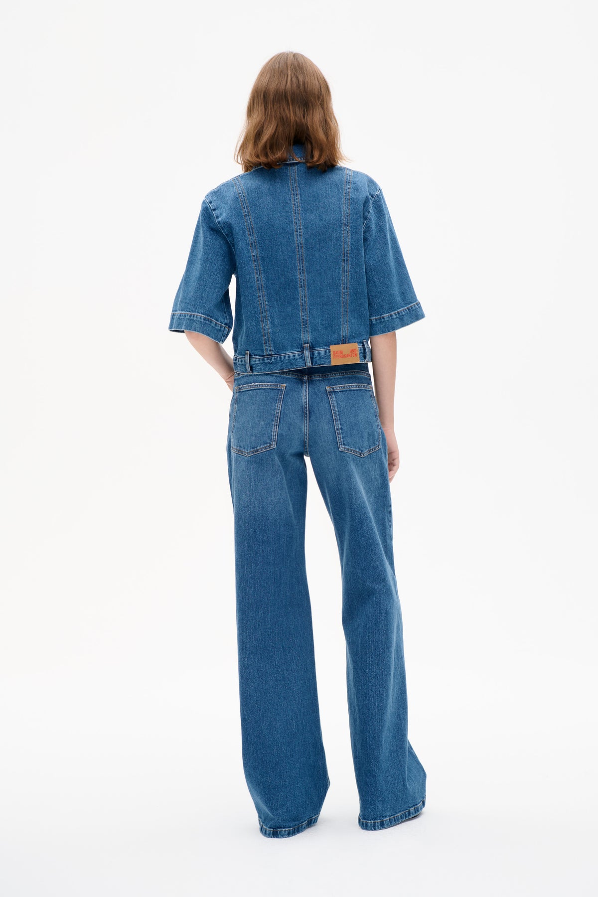Rückenansicht eines Models, das eine blaue denim-Jacke mit weiten, kurzen Ärmeln und eine dazu passende, weit geschnittene Jeans trägt.